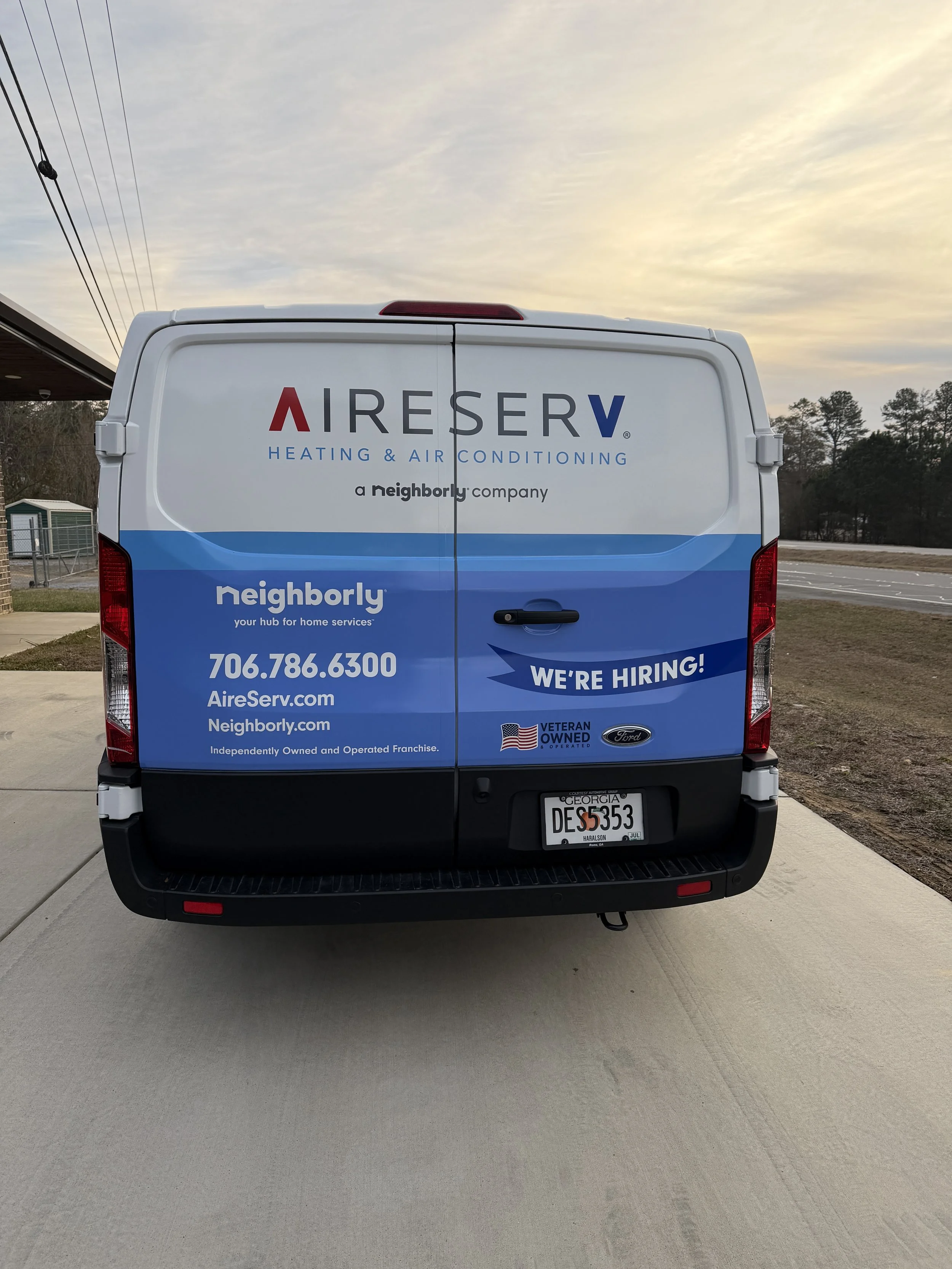 Back of a company service van with advertising for Aire Serv Heating & Air Conditioning and Neighborly, displaying contact information and a 'We're Hiring!' message.