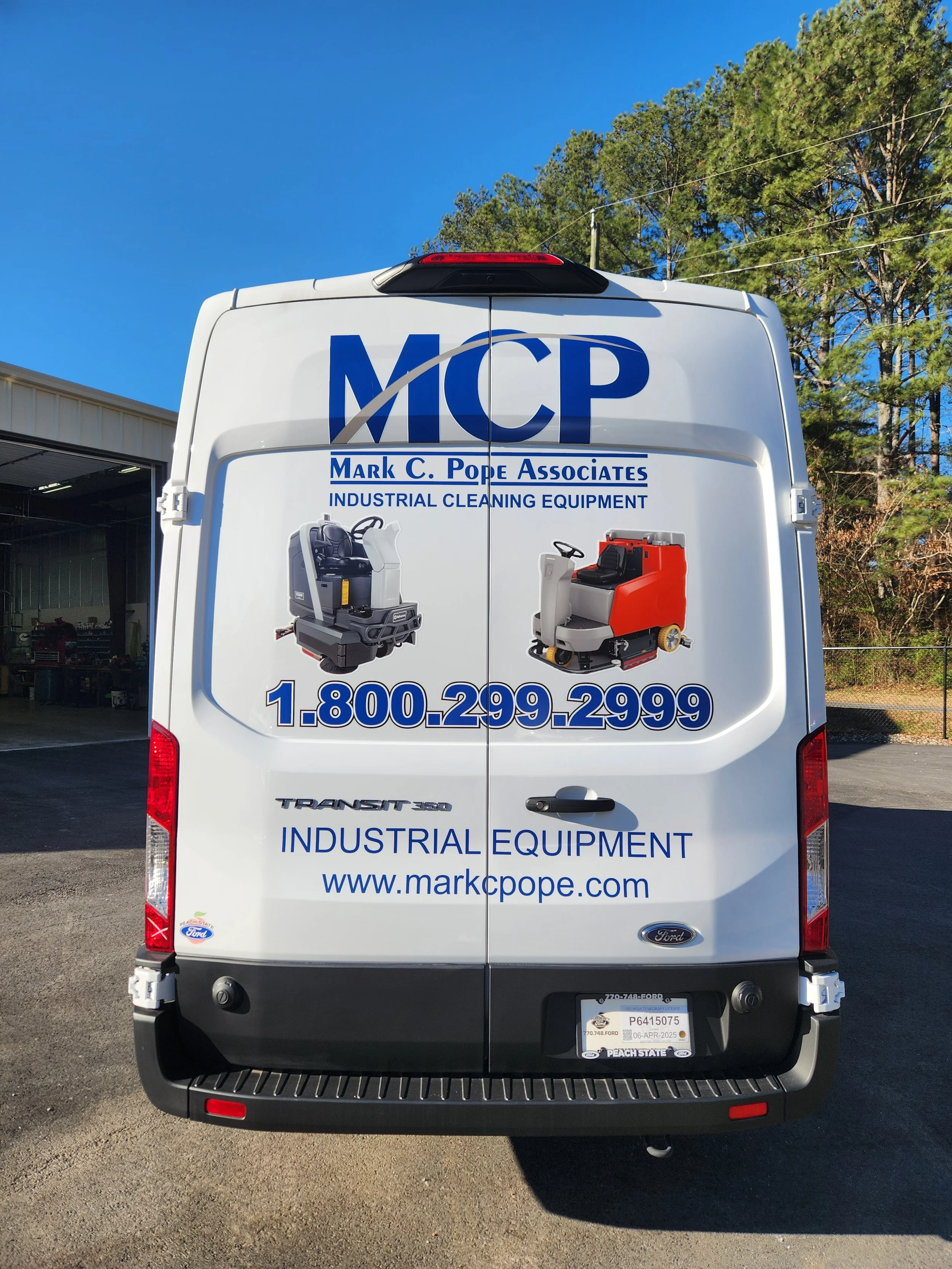 Rear view of a white utility van with advertisements for Mark C. Pope Associates, industrial cleaning equipment, and contact information. The van displays images of cleaning machines, phone number 1-800-299-2999, and website www.markcpope.com.