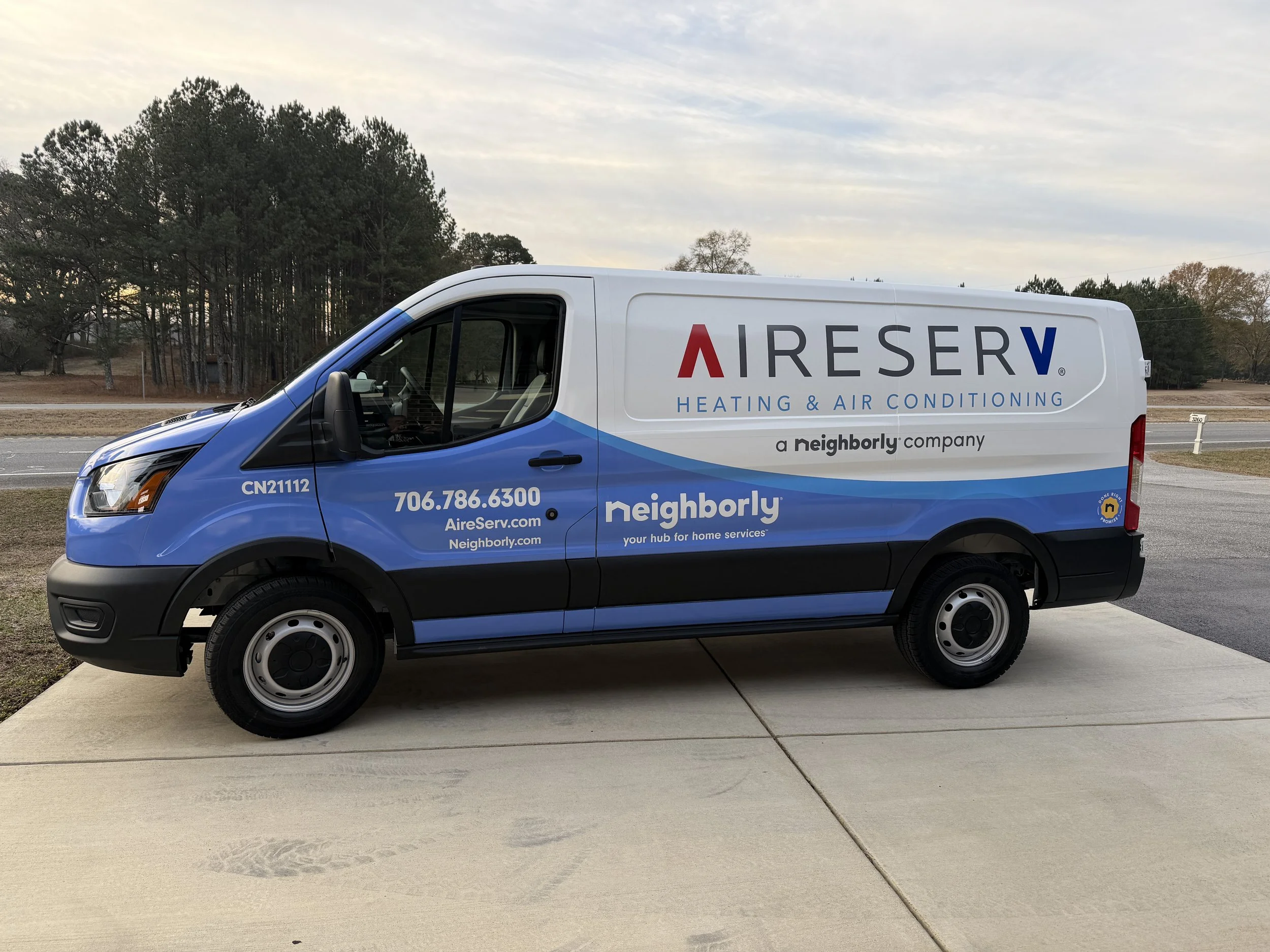 Company van parked on driveway, blue and white with logos and contact information for AireServ heating and air conditioning, Neighborly company.