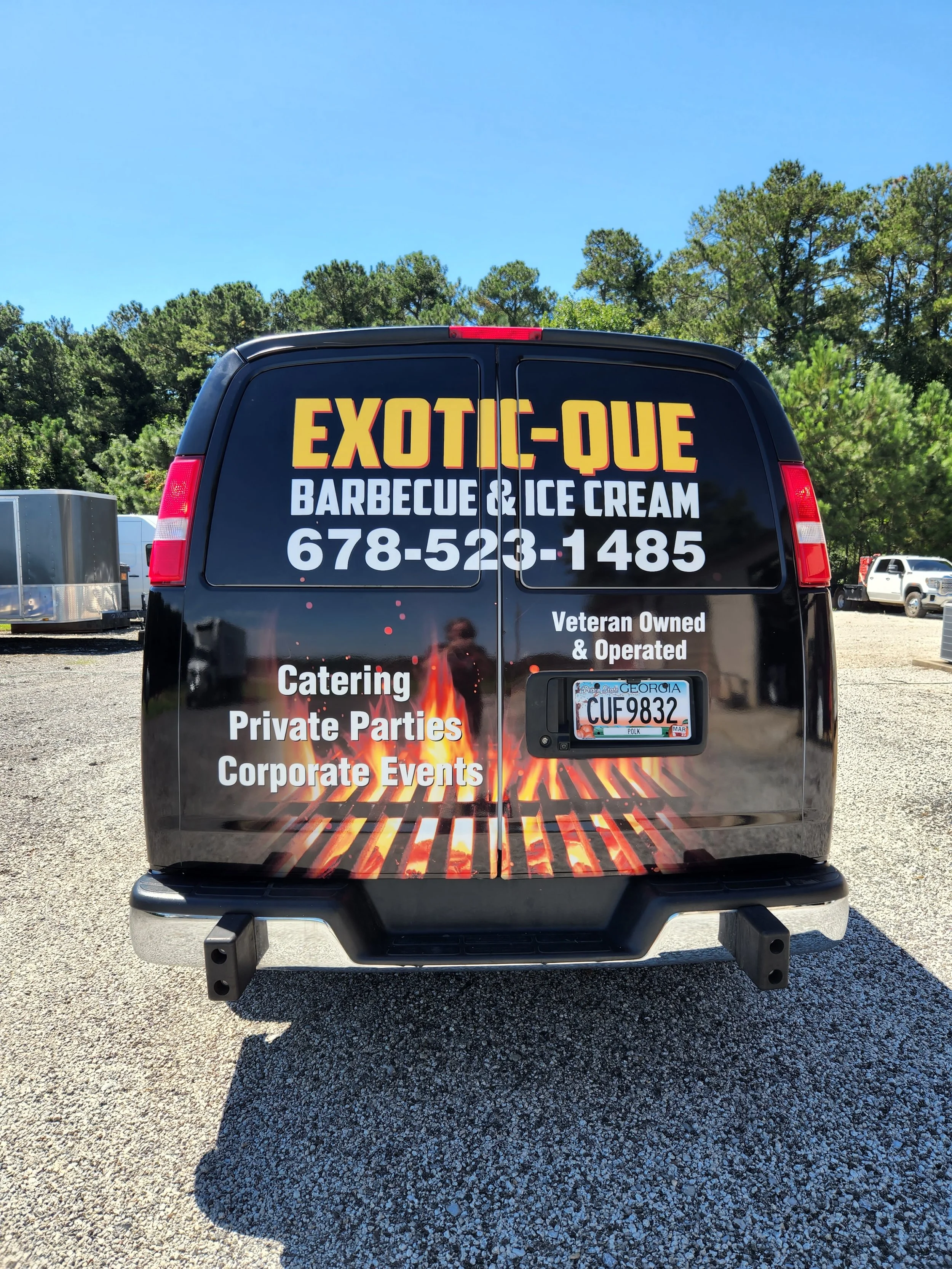 The back of a black van advertising Exoti-Que barbecue and ice cream, with a fiery grill graphic at the bottom, Georgia license plate, and contact information.