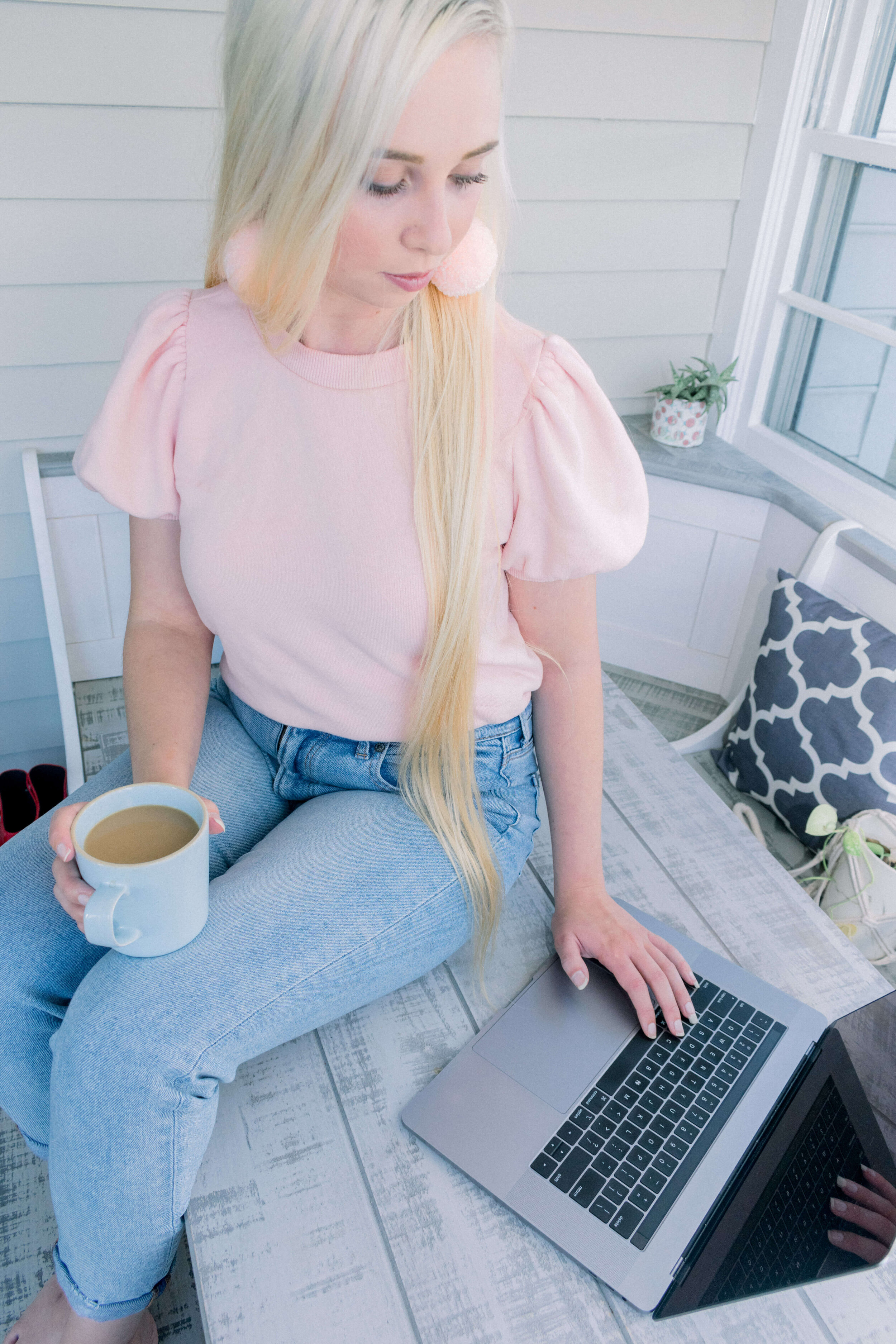 Kenzi Green Website Designer sitting on table drinking coffee working on laptop