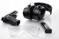Pistol, hearing protection earmuffs, safety glasses, and magazine on white background.