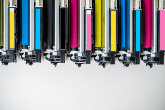 A row of color printer toner cartridges in blue, black, pink, yellow, and cyan, arranged horizontally against a white background.