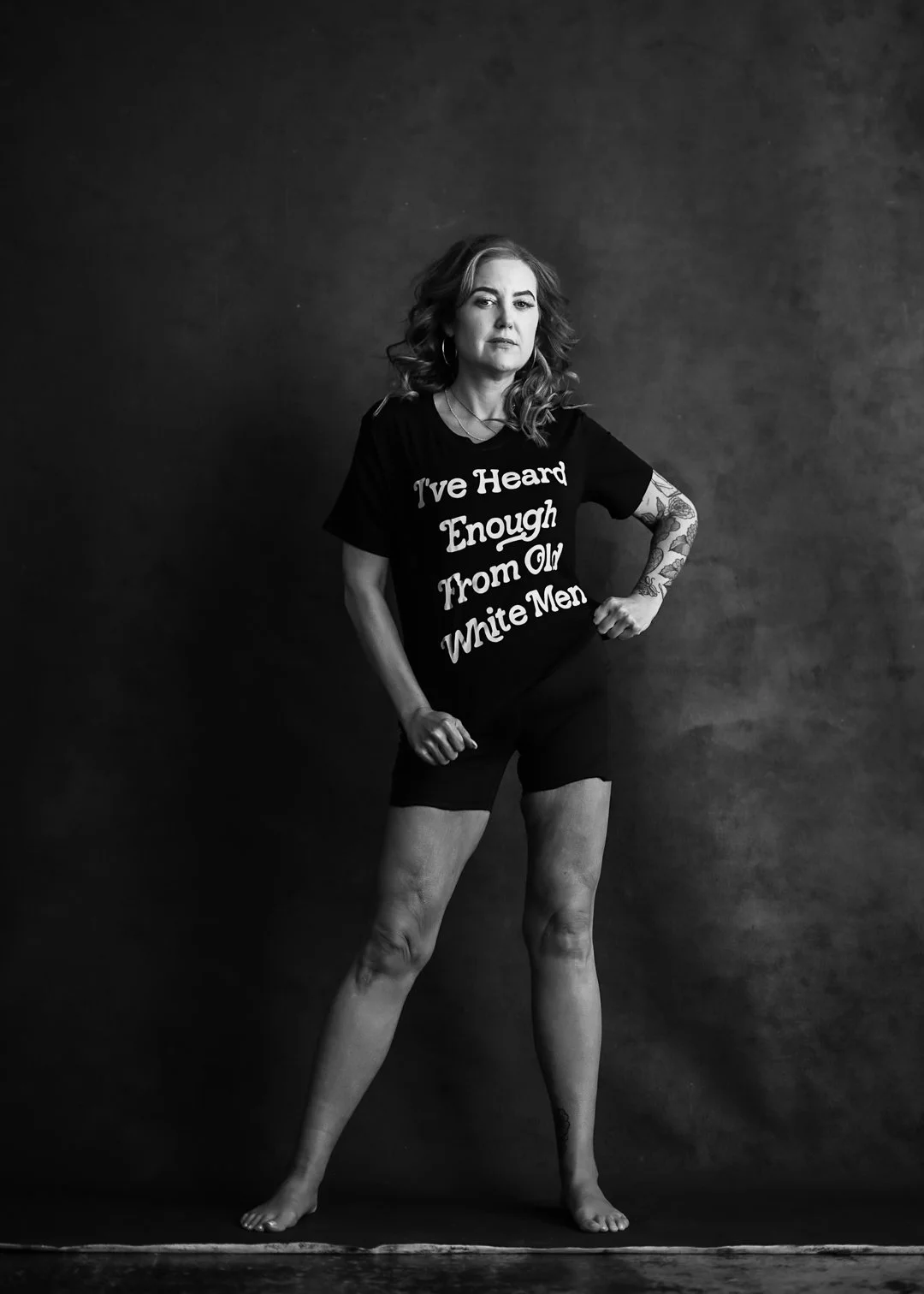 Black and white portrait photography of a confident middle aged woman, wearing a t-shirt that says: "I'm tired of listening to old white men"