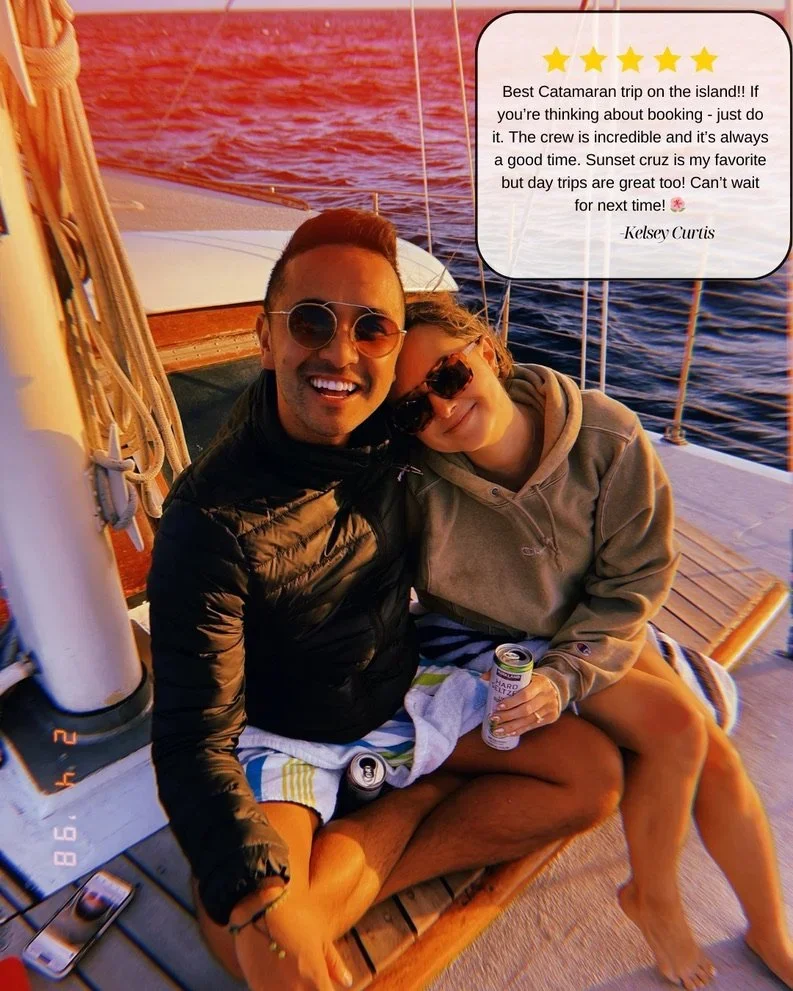 Two people sitting together on a boat at sunset, smiling and enjoying themselves. The man is wearing sunglasses and a black jacket, while the girl is wearing sunglasses and a hoodie, holding a can of drink. The water in the background is reflecting the sunset colors, creating a warm, picturesque scene.