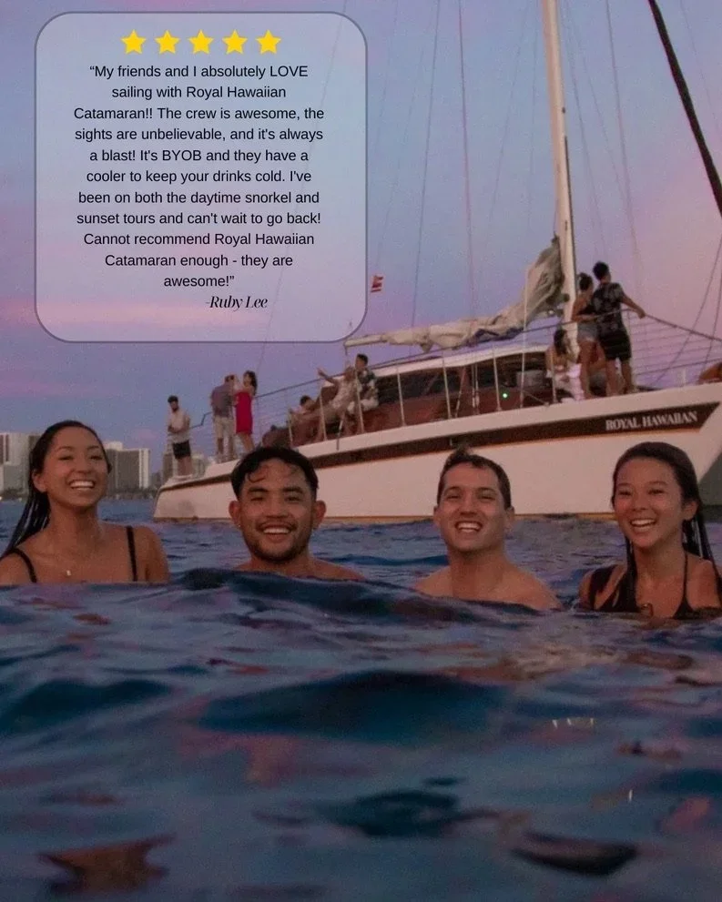 Four people smiling and swimming in the water near a sailboat named Royal Hawaiian, with a sunset sky in the background and a group of people on the boat.