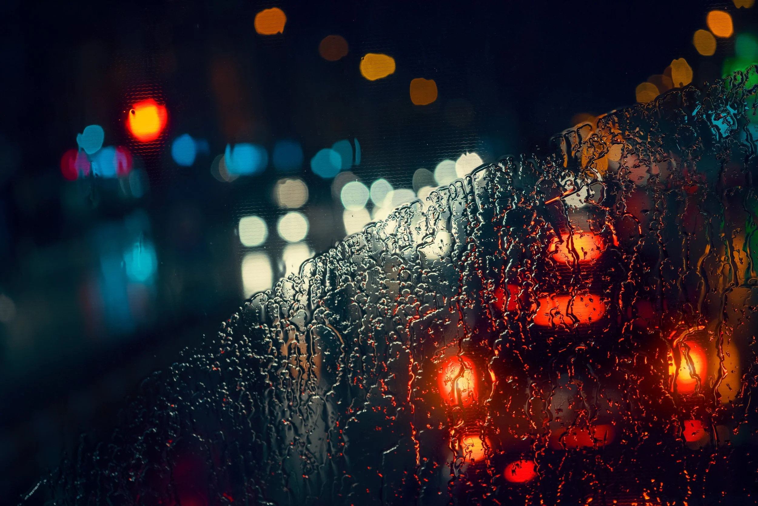 Traffic and vehicle lights blurred through a rain-covered windshield at night.