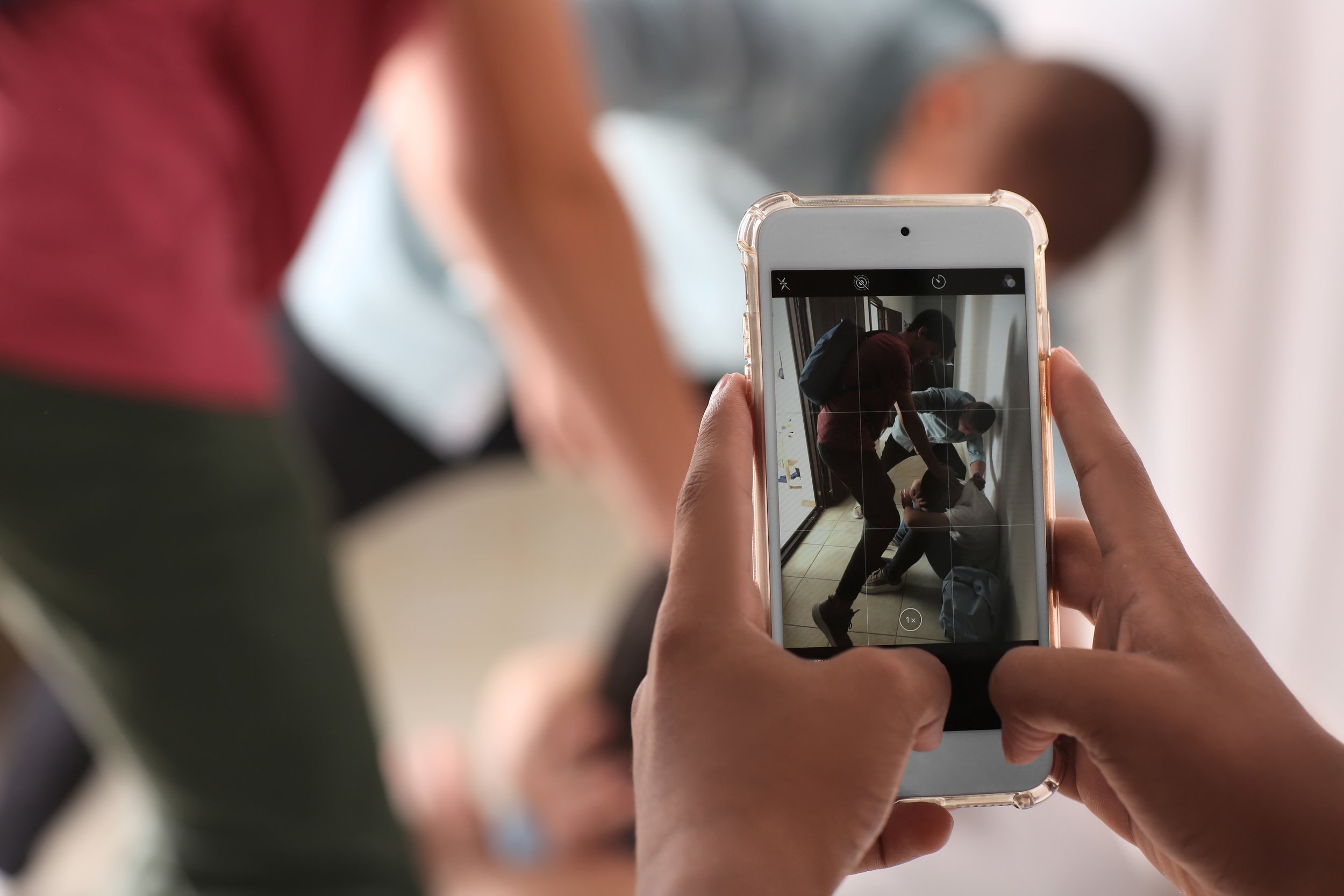 A smartphone records students physically bullying another student in a school hallway.