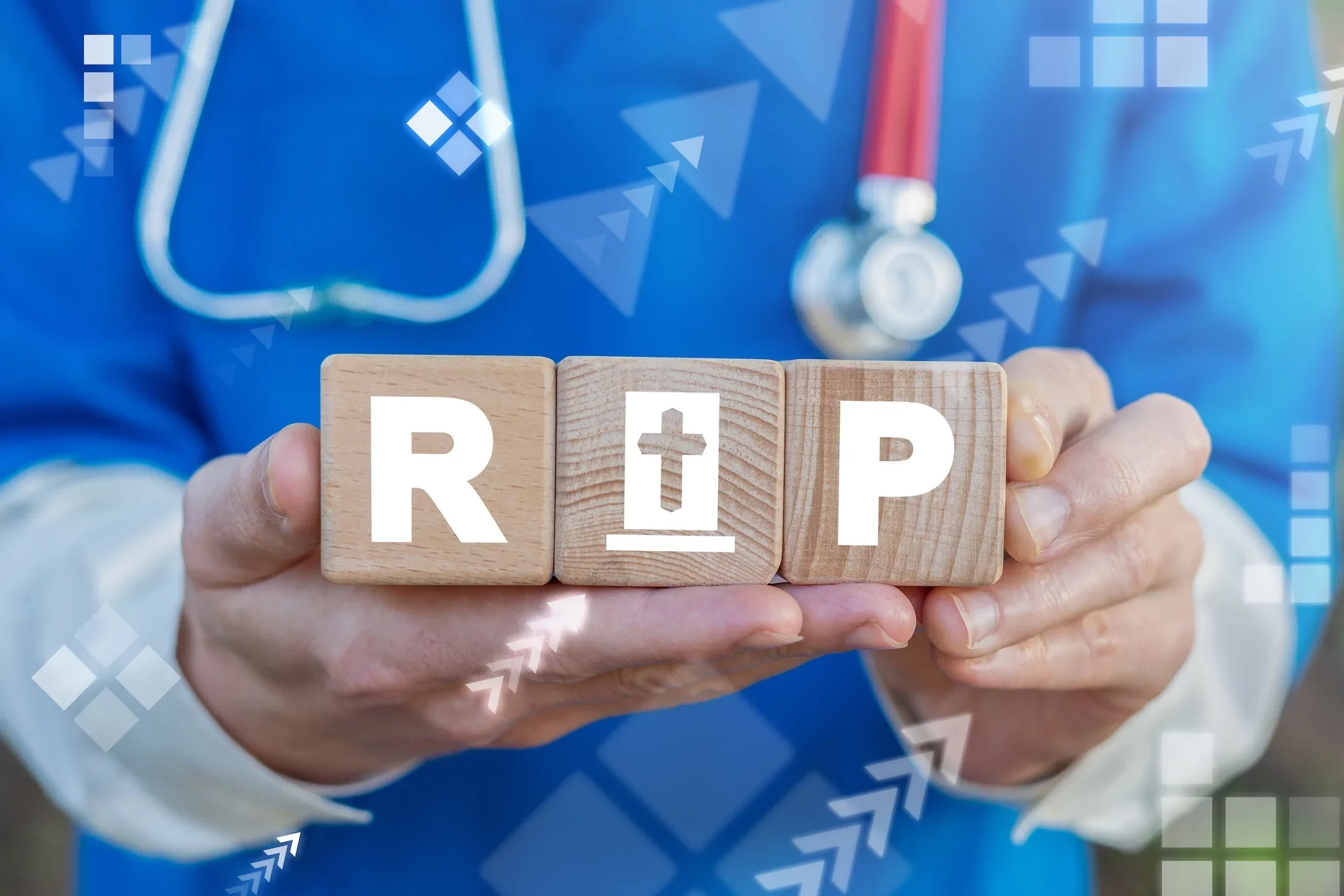 A healthcare worker in blue scrubs and a stethoscope holding wooden blocks spelling R.I.P with a cross symbol, representing death or end of life.
