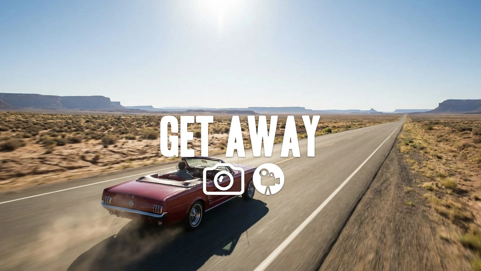 Wide shot of a classic convertible speeding across a vast, empty American desert road. Freedom, bright sunlight, no music.