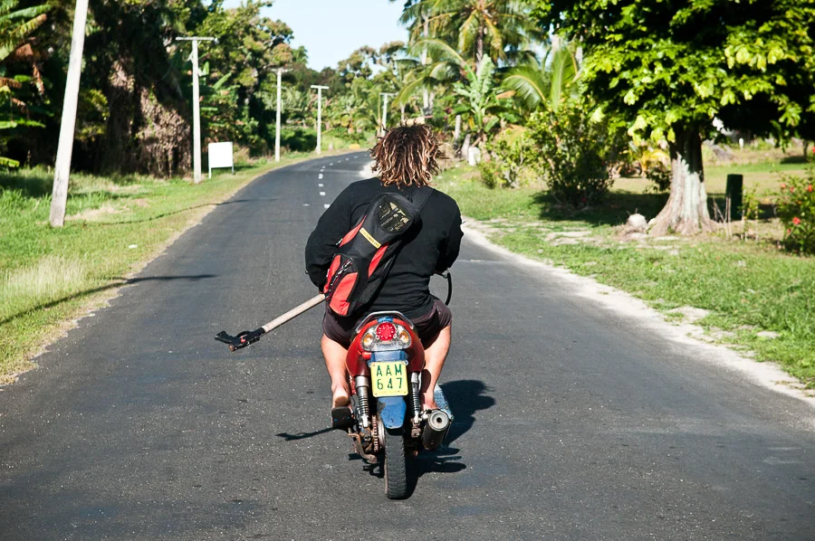 Spear fisherman carrying his spear gun while riding his scooter, Aitutaki, Cook Islands.
