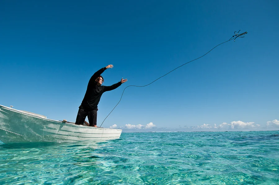 A spear fisherman throwing his boats anchor into a lagoon, Aitutaki, Cook Islands.
