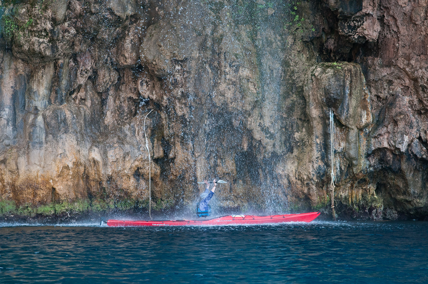 Woman sea kayaker paddling under a water fall, Turquoise Coast Turkey.
