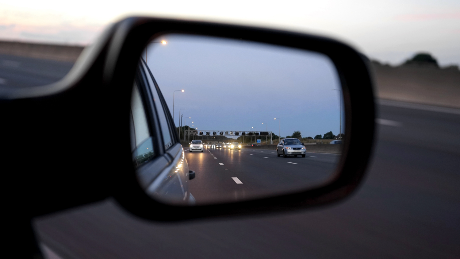 passenger side mirror on car shows a rear view reflection of cars on highway