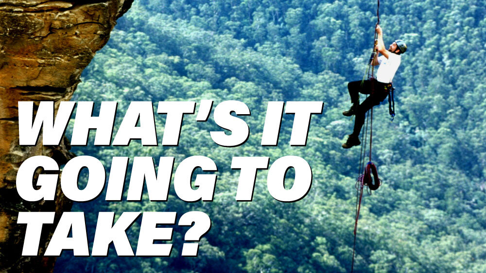 Man climbs a rock face above a forrest. 'What's it going to take' is super imposed
