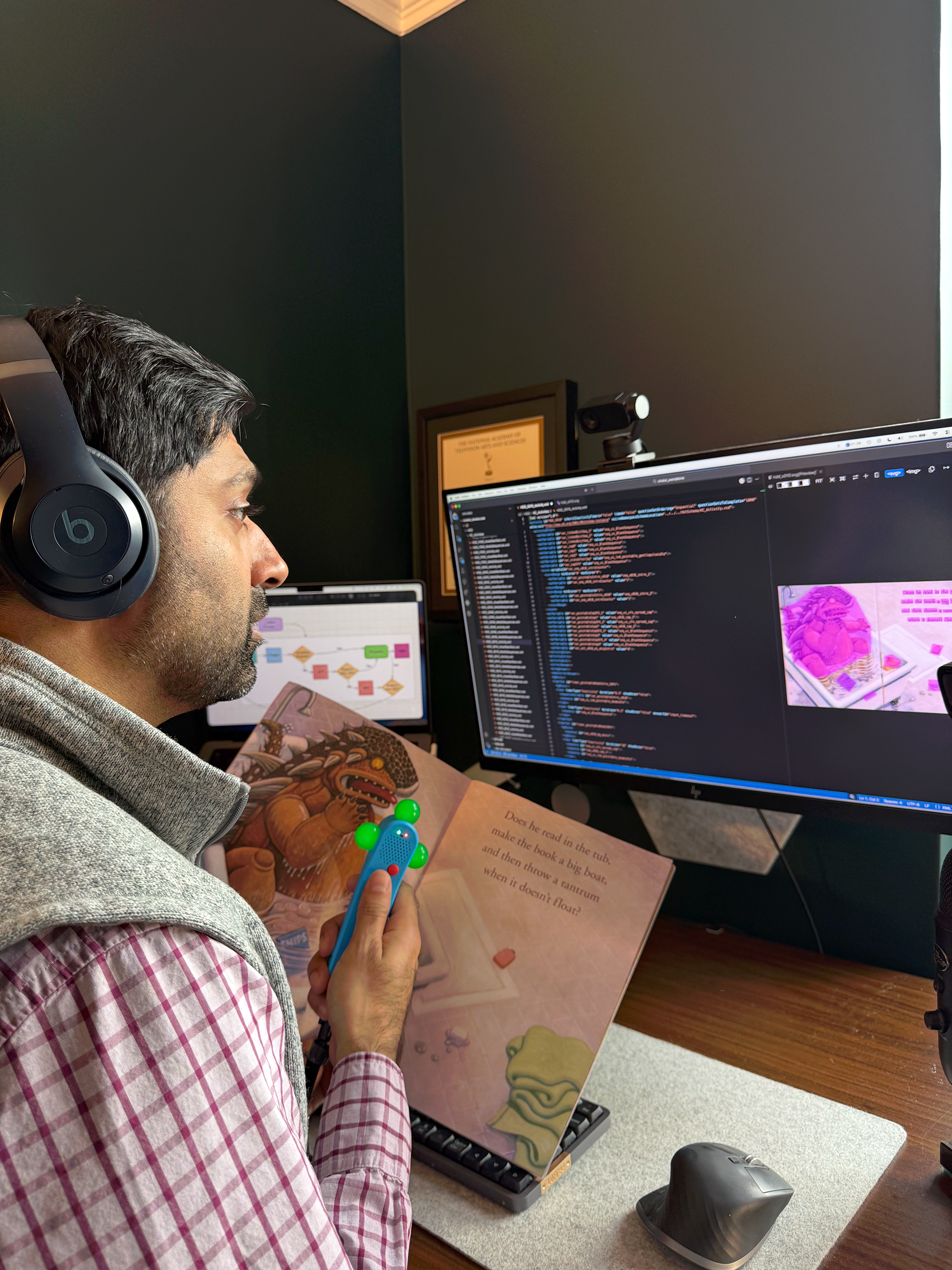 Saurin Choksi at desk with headphones, working on code while holding Kibeam wand and children's book