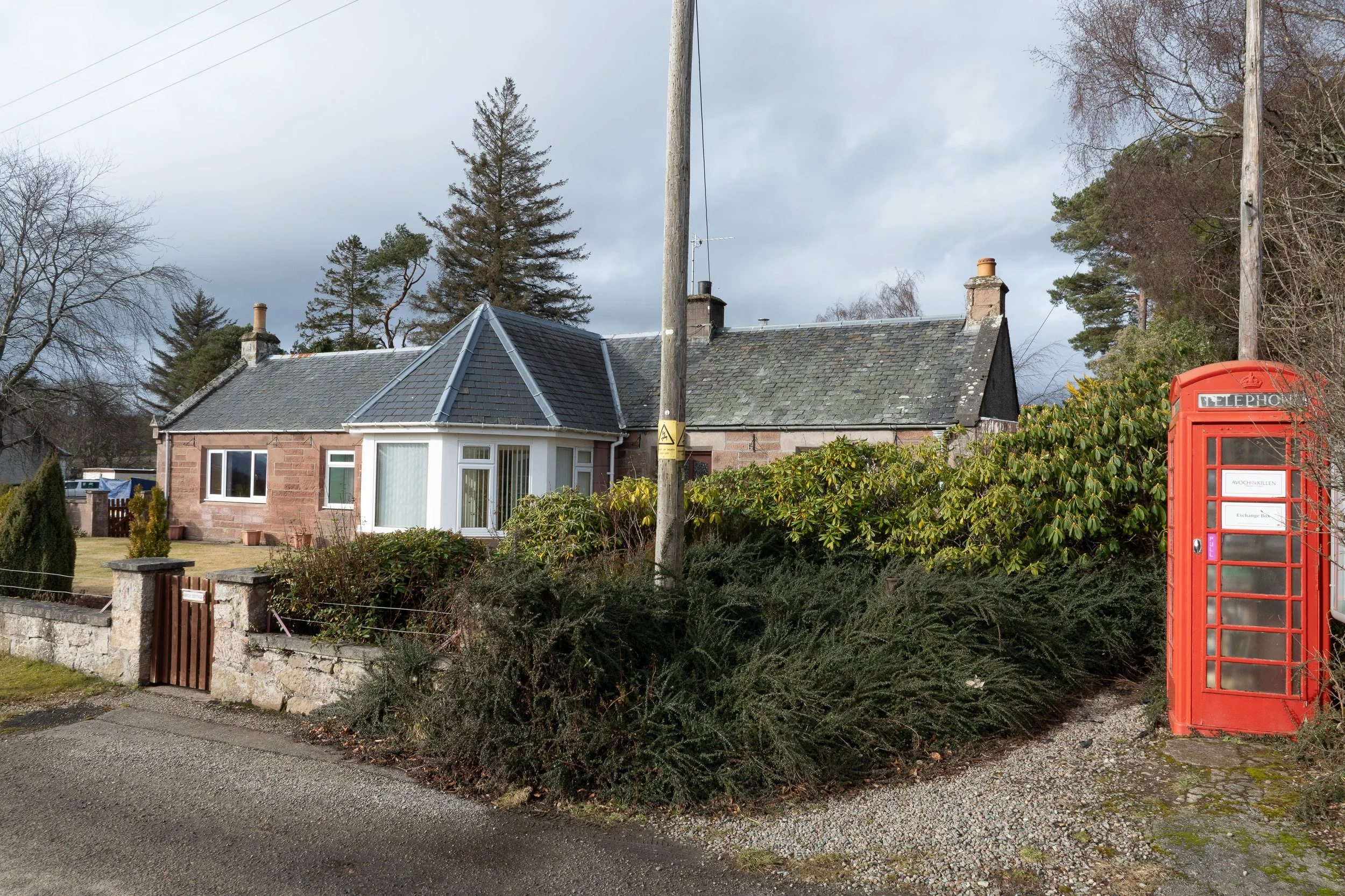 Exterior lifestyle photograph of a Highland cottage on the Black Isle with an old phonebox outside.