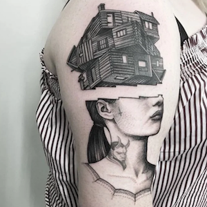 Tattoo of a woman with a bob haircut and a cat on her shoulder, and a house above her head on the upper arm