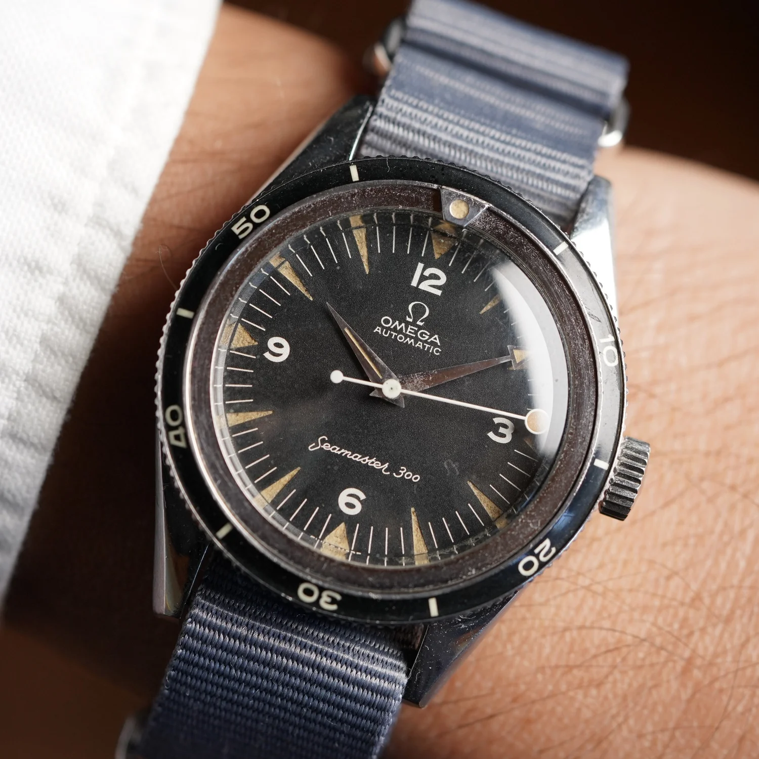 Wrist shot of a CK2913-8 on a grey NATO strap: lollipop seconds hand, pointed hour and arrow-tipped minute hands, black dial with triangle indexes and Arabic numerals, thin Bakelite bezel. The listing also shows the caseback stamped 2913-8 SC. · Photo: Wind Vintage · © Wind Vintage, used with permission · Source: https://www.windvintage.com/omega-seamaster-300-reference-ck-2913