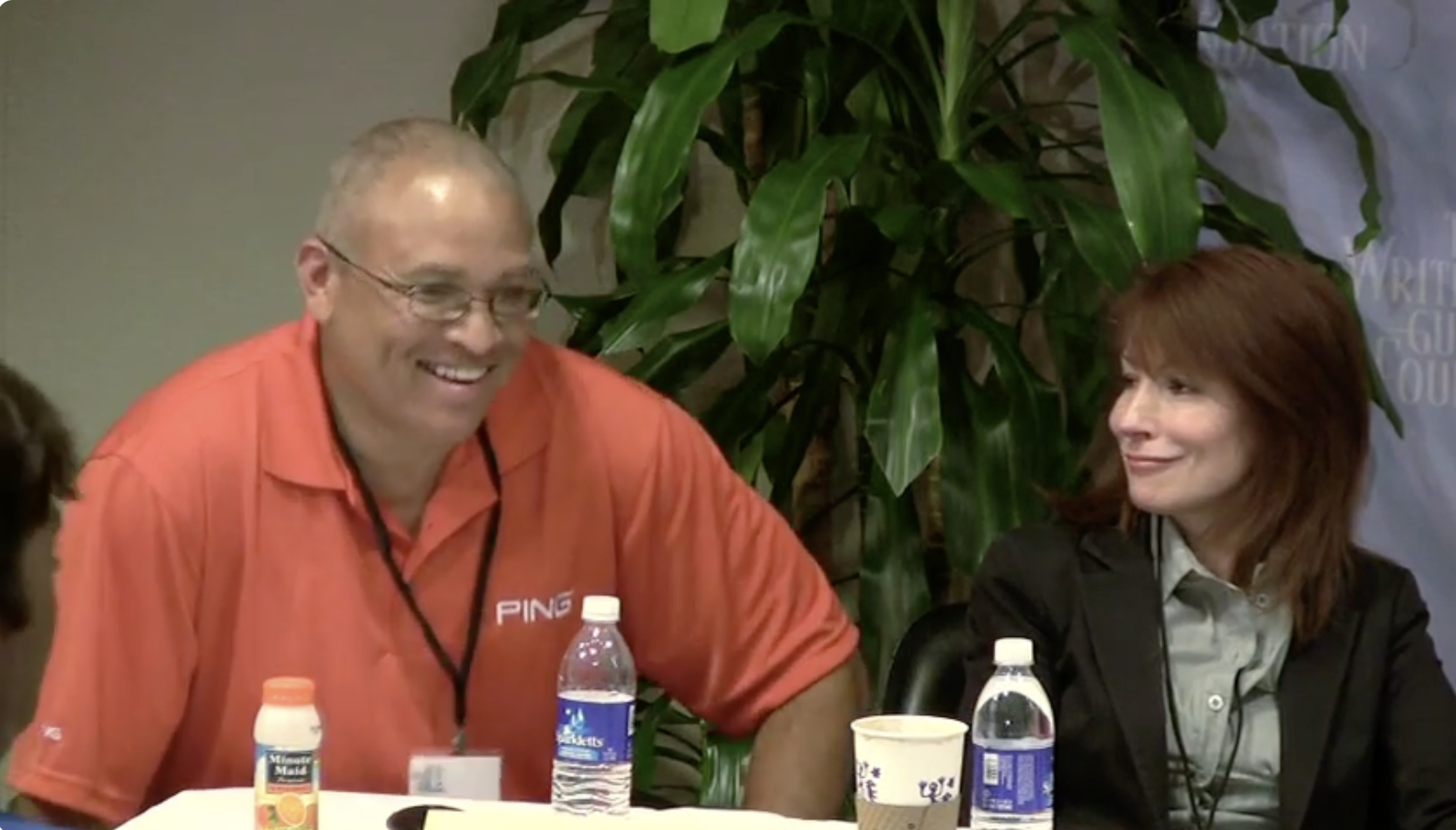 Two writers at panel with water bottles and coffee in front of them