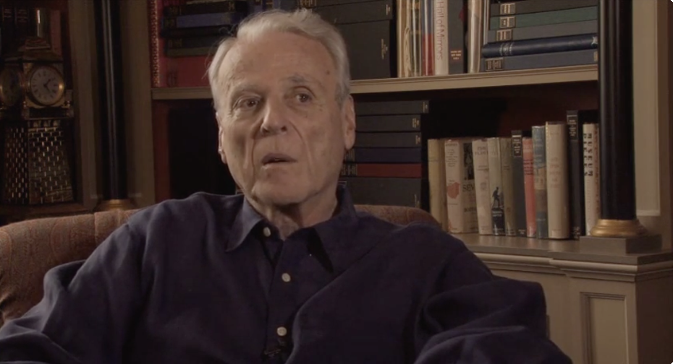 William Goldman seated for his interview with a bookcase behind him.