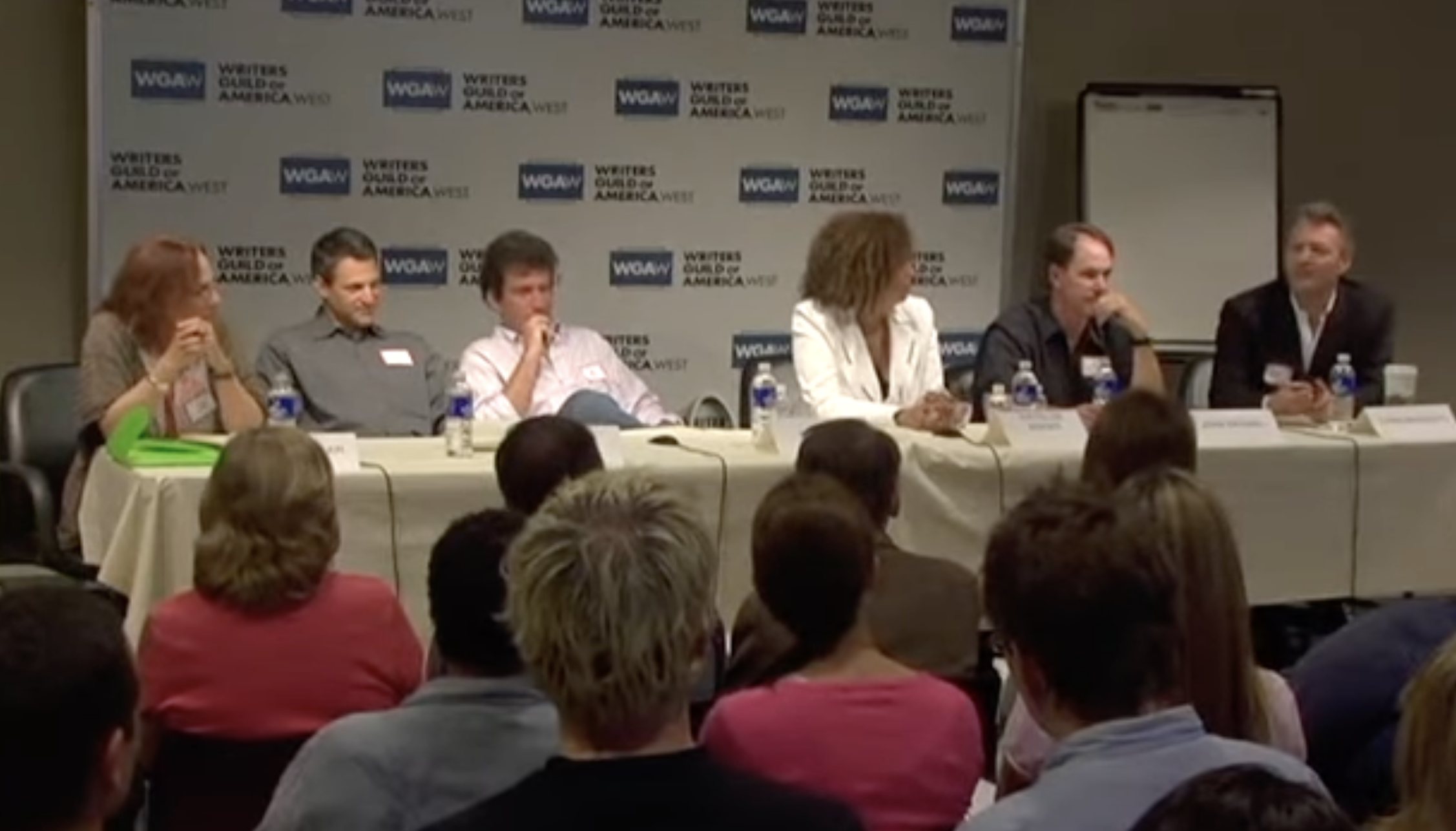 Panel of writers at long table with white tablecloth and folks in the audience looking at them