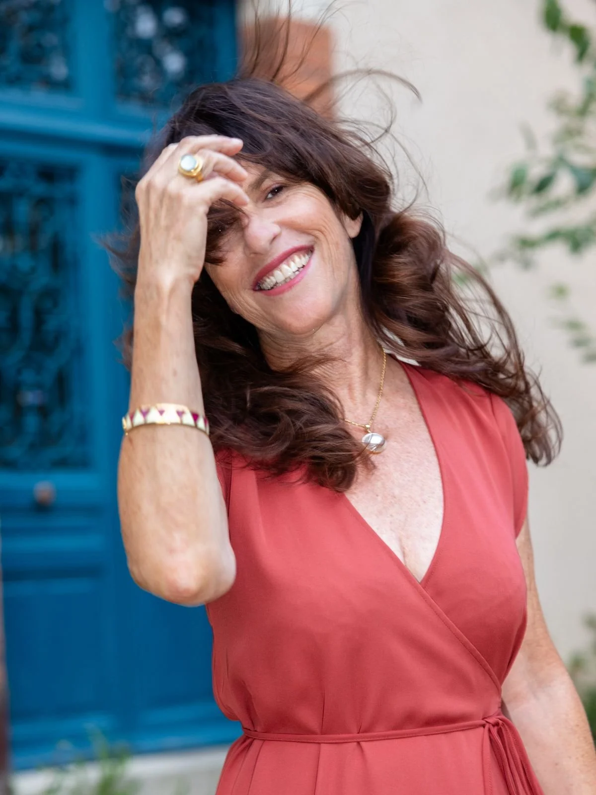 A smiling woman with long, curly brown hair in a red sleeveless dress.