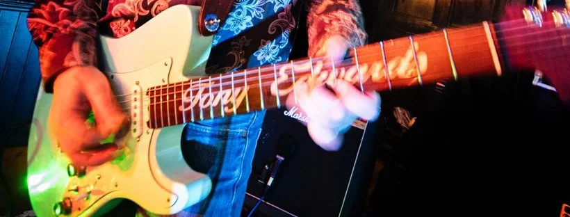 Close-up of a person playing an electric guitar with a colorful background.
