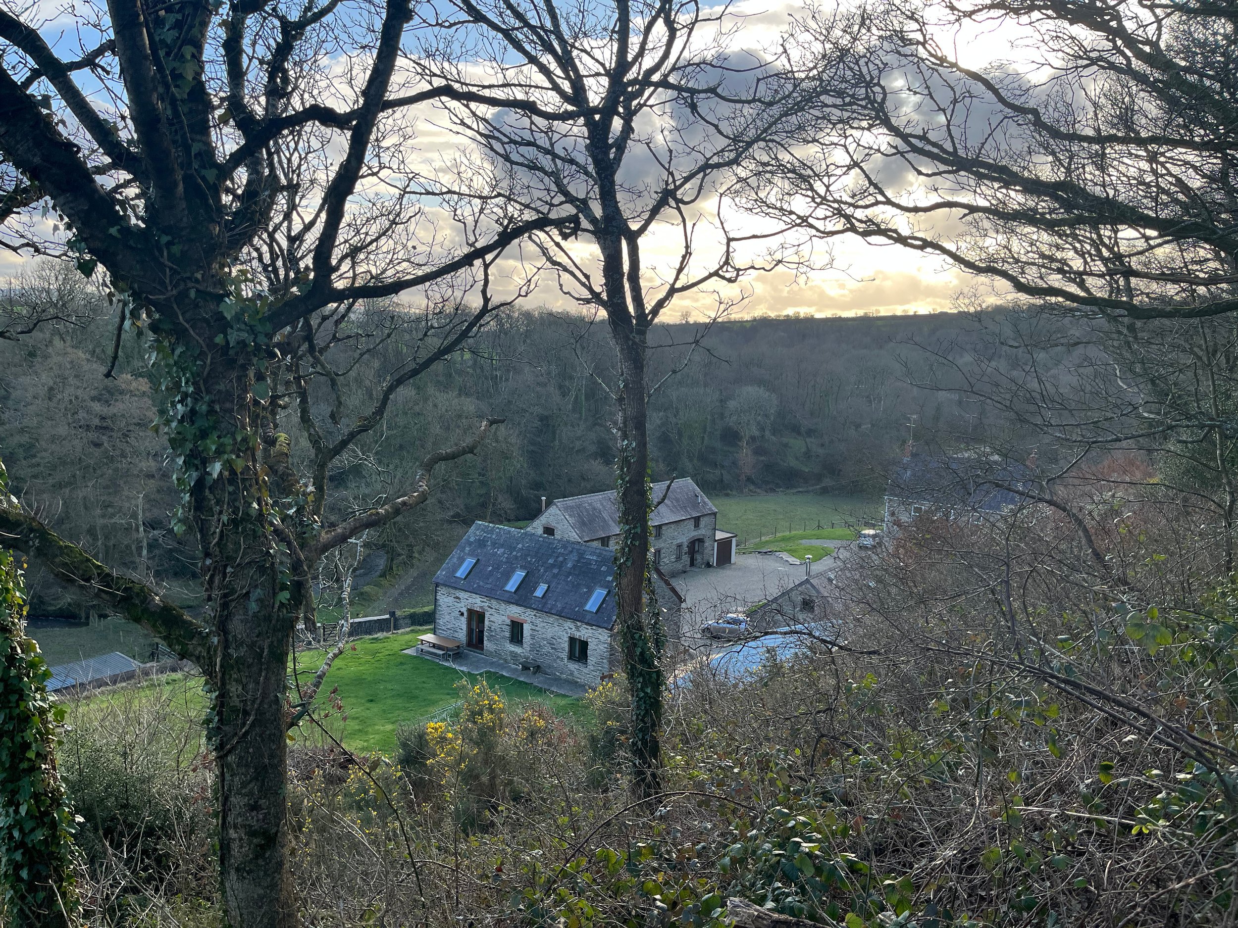 A view of a rural landscape with leafless trees, a cloudy sky, and a few houses with gray roofs in the distance.