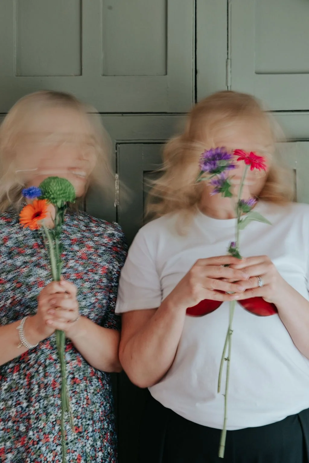 two women shaking their heads in a blur holding bright flowers they teach marketing to florists