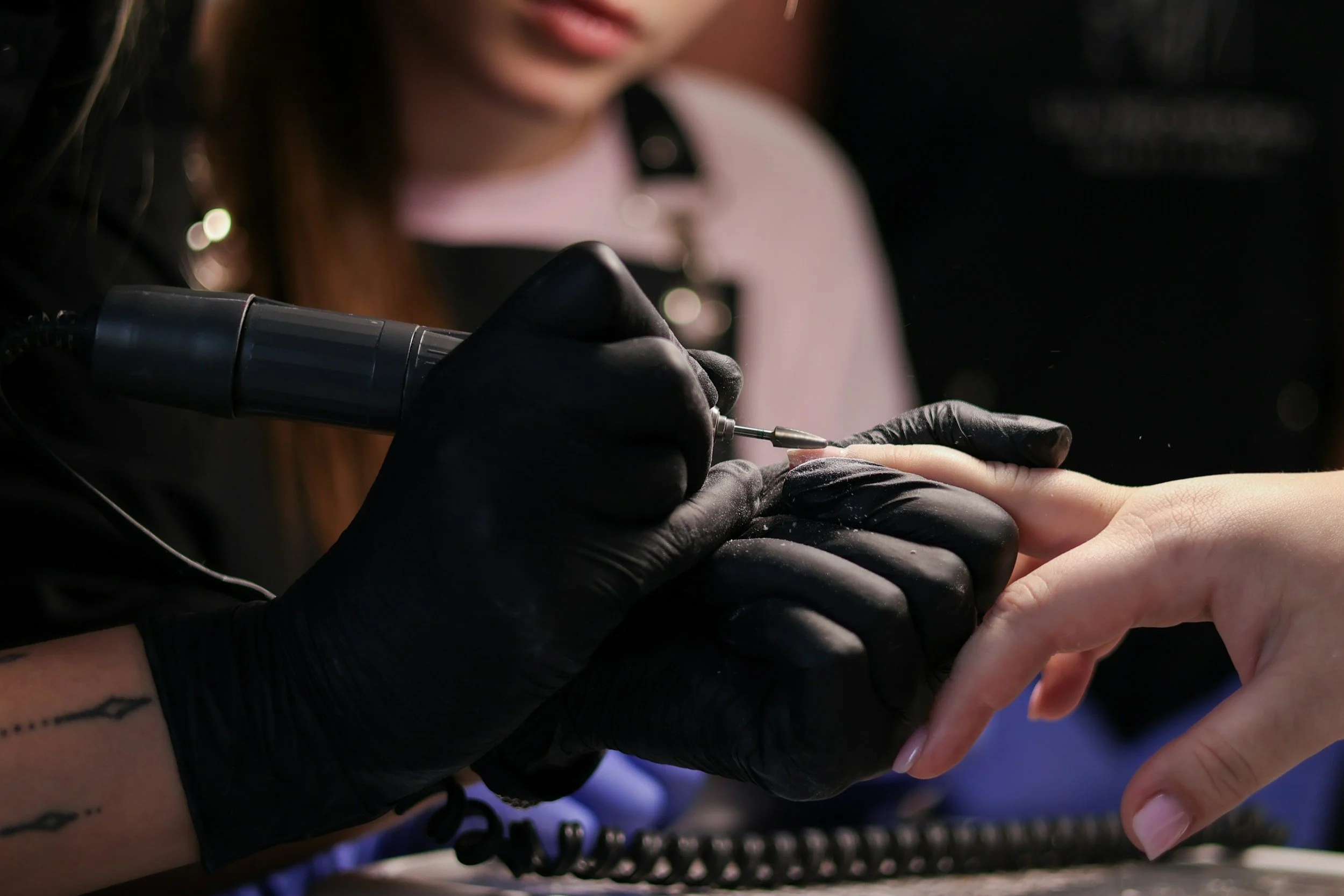 A tattooed hand wearing a black glove is using a tattoo machine to ink a design on a person's finger.