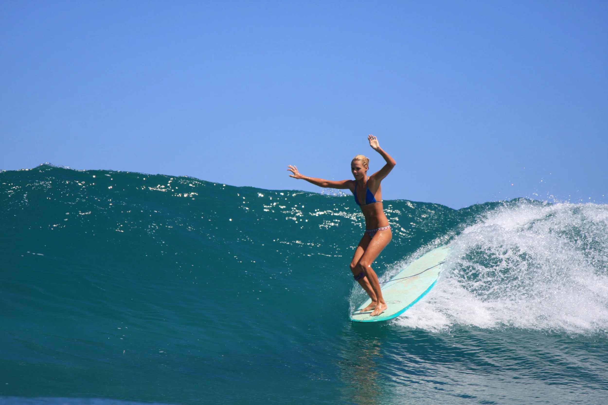 A woman surfing on a wave in the ocean wearing a blue bikini.