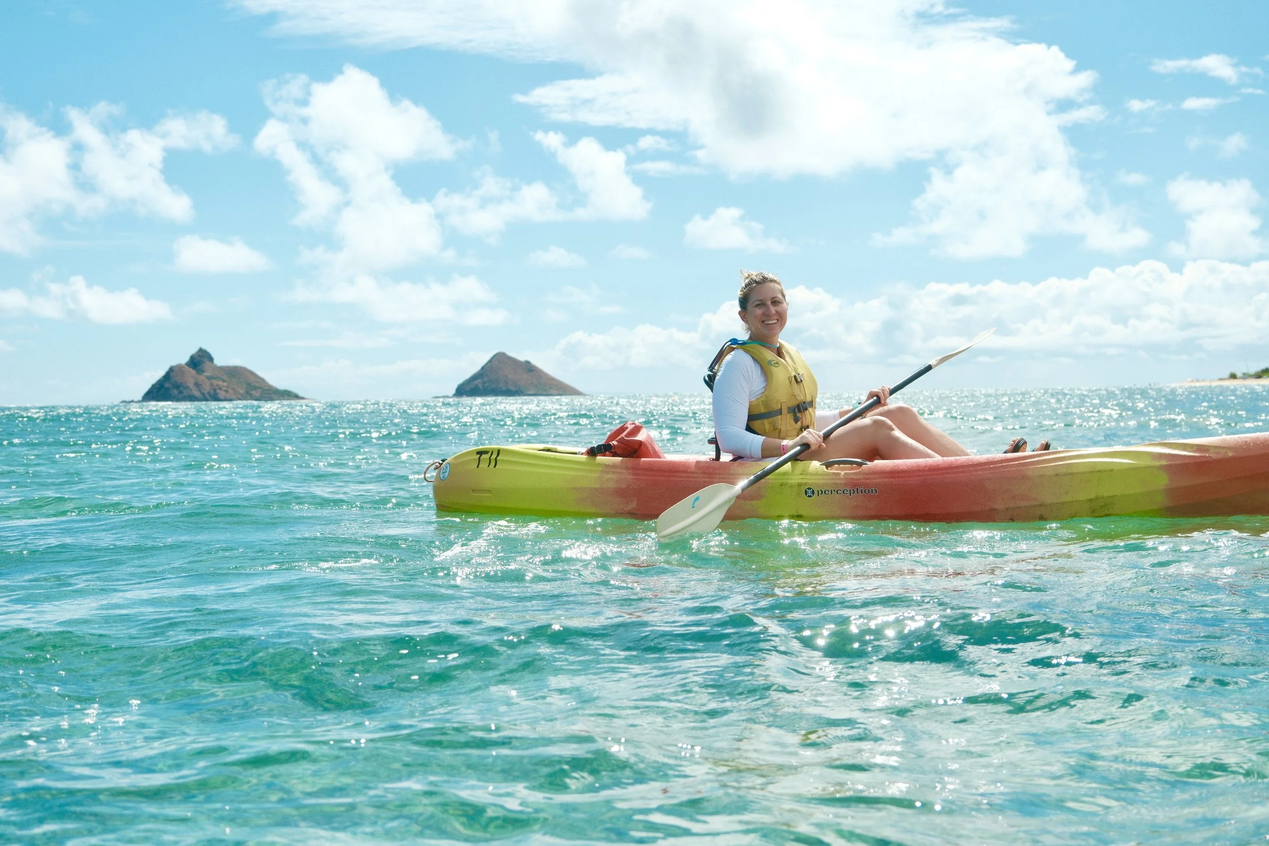Woman kayaking on the ocean with small islands in the background and a partly cloudy sky.