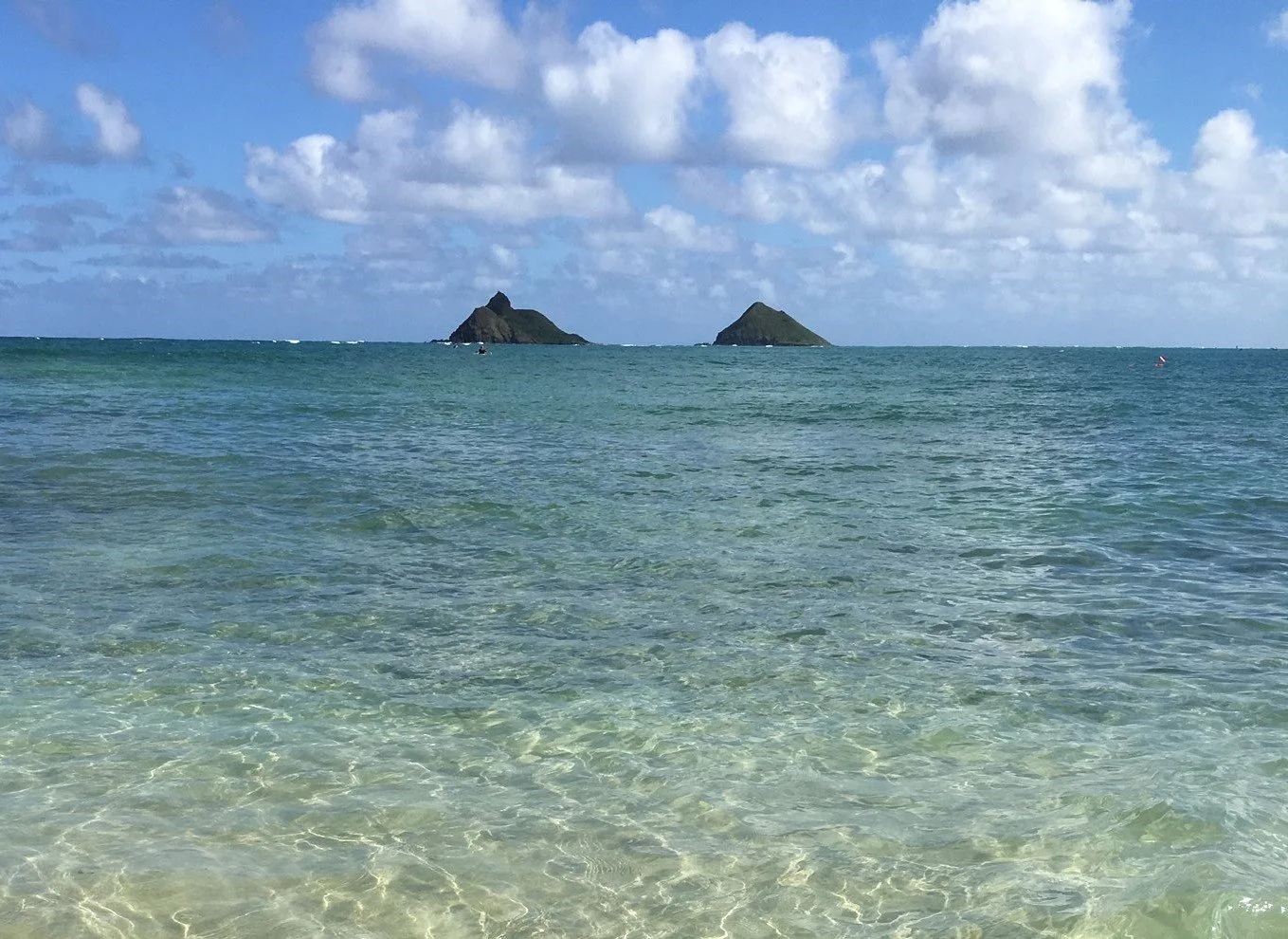 Two small islands in the ocean with rocky peaks, under a partly cloudy sky.