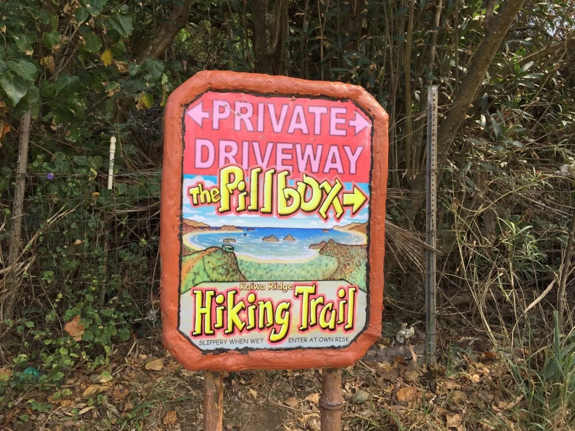 Colorful sign for a hiking trail at Kaiwa Ridge titled 'The Pill Box,' with a scenic illustration of a coastline and the words 'Private Driveway' at the top.