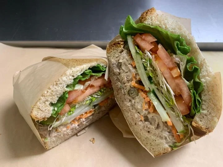Close-up of a partially unwrapped sandwich cut in half, showing lettuce, tomato, sliced turkey, and shredded carrots on whole wheat bread.