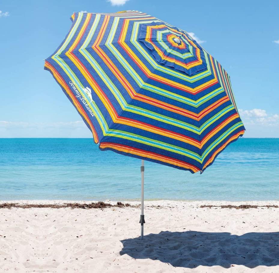 Colorful striped beach umbrella on sandy shore with ocean and sky in background.