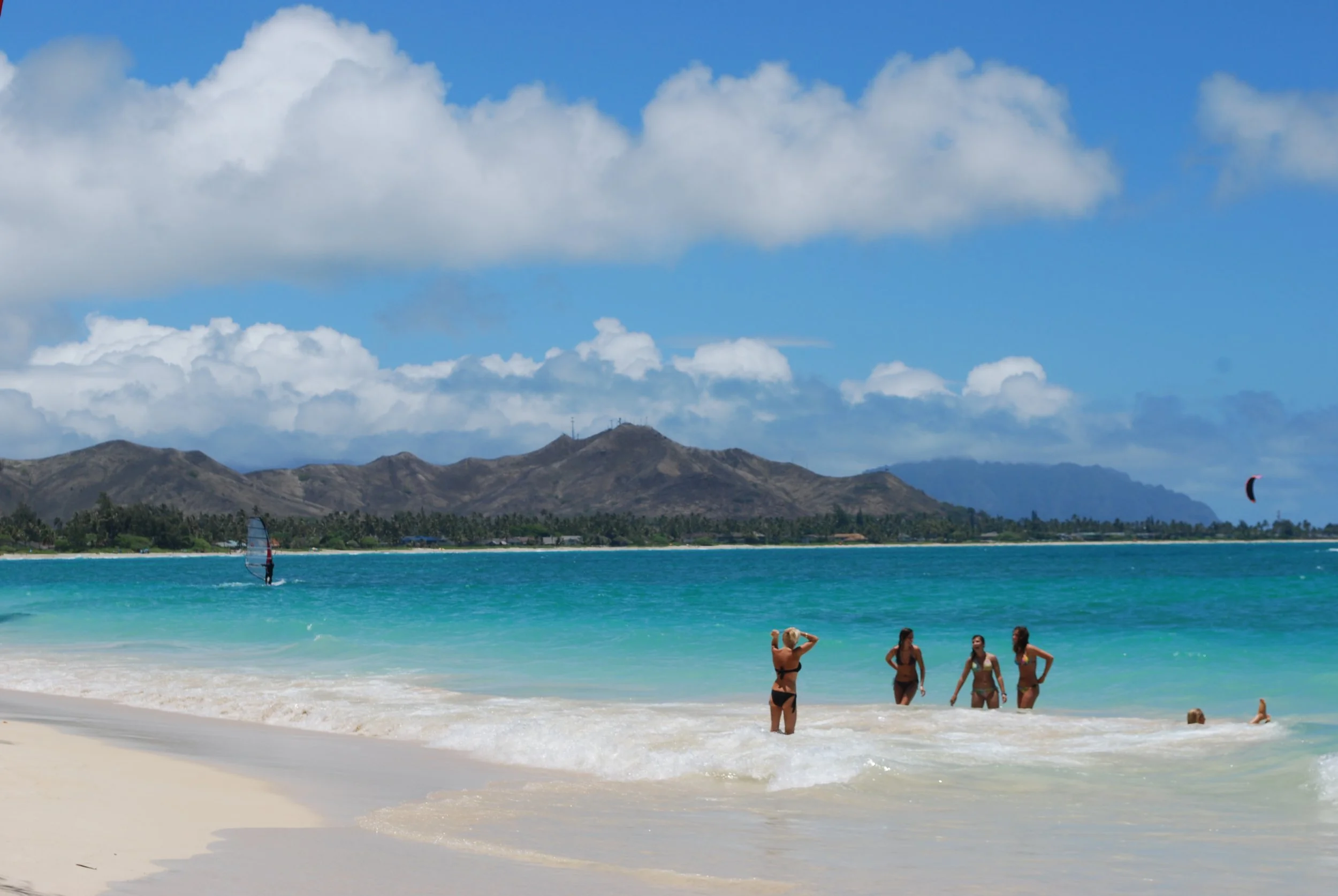 People swimming in the ocean with mountains and cloudy sky in the background
