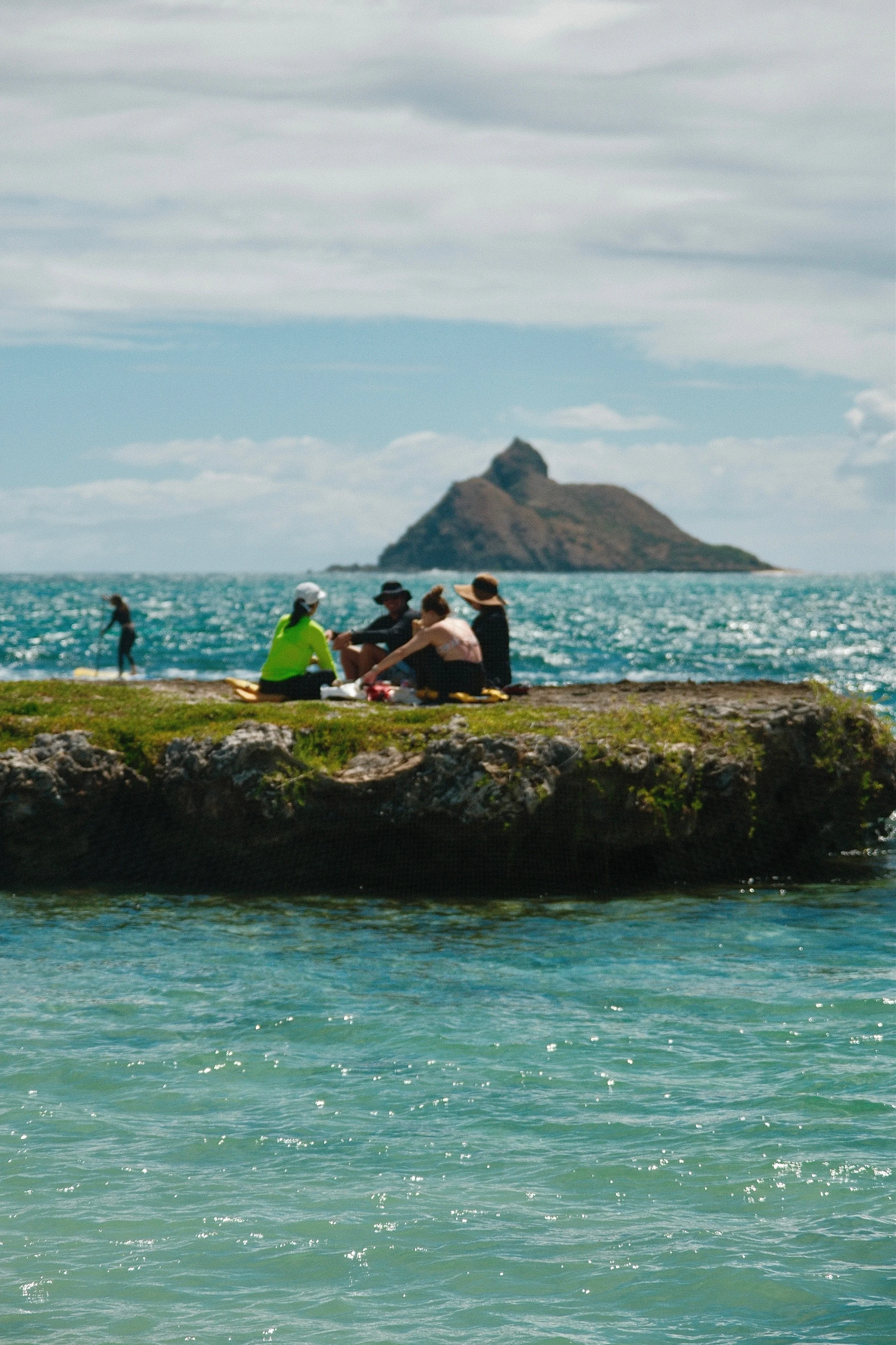 A group of five people sitting on flat island in kailua bay having lunch
