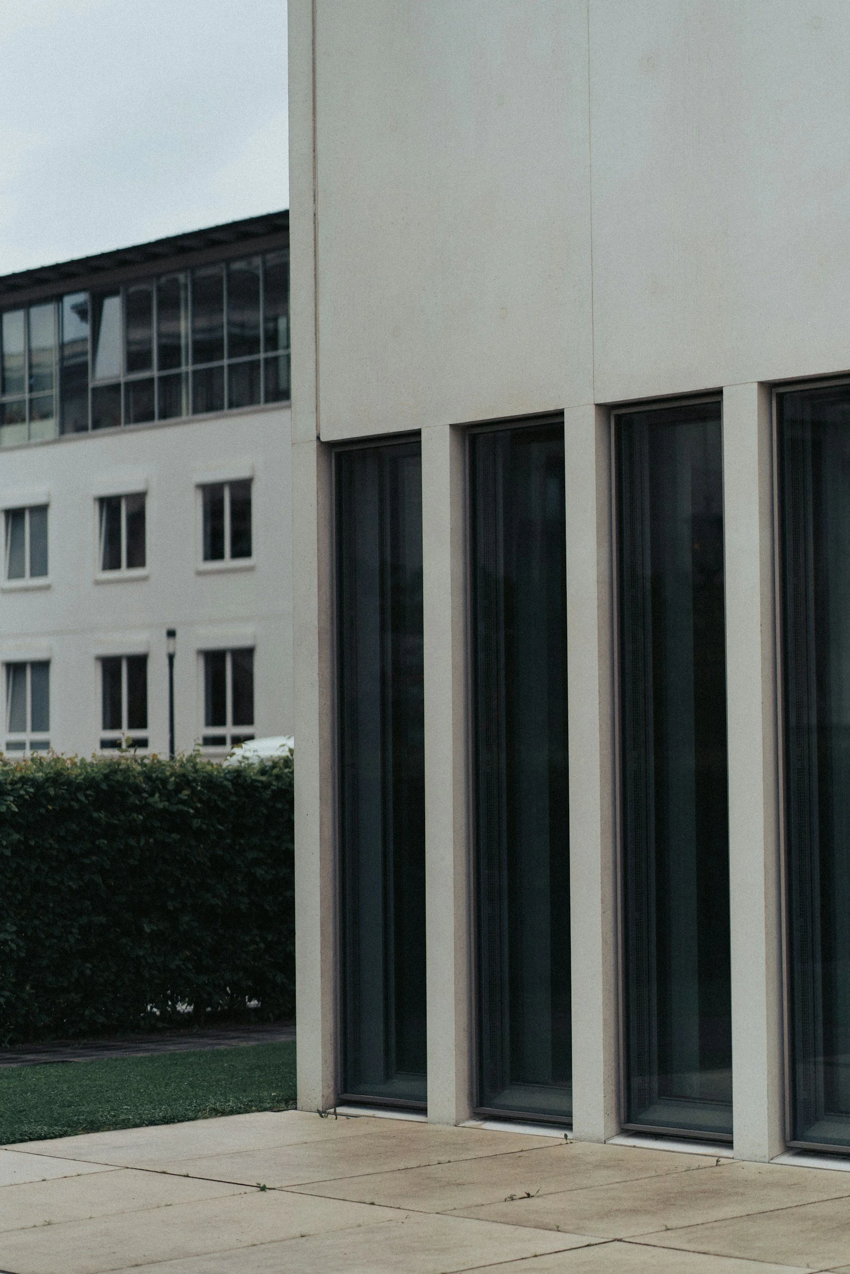 Exterior of a modern building with large glass windows and a concrete sidewalk in front.