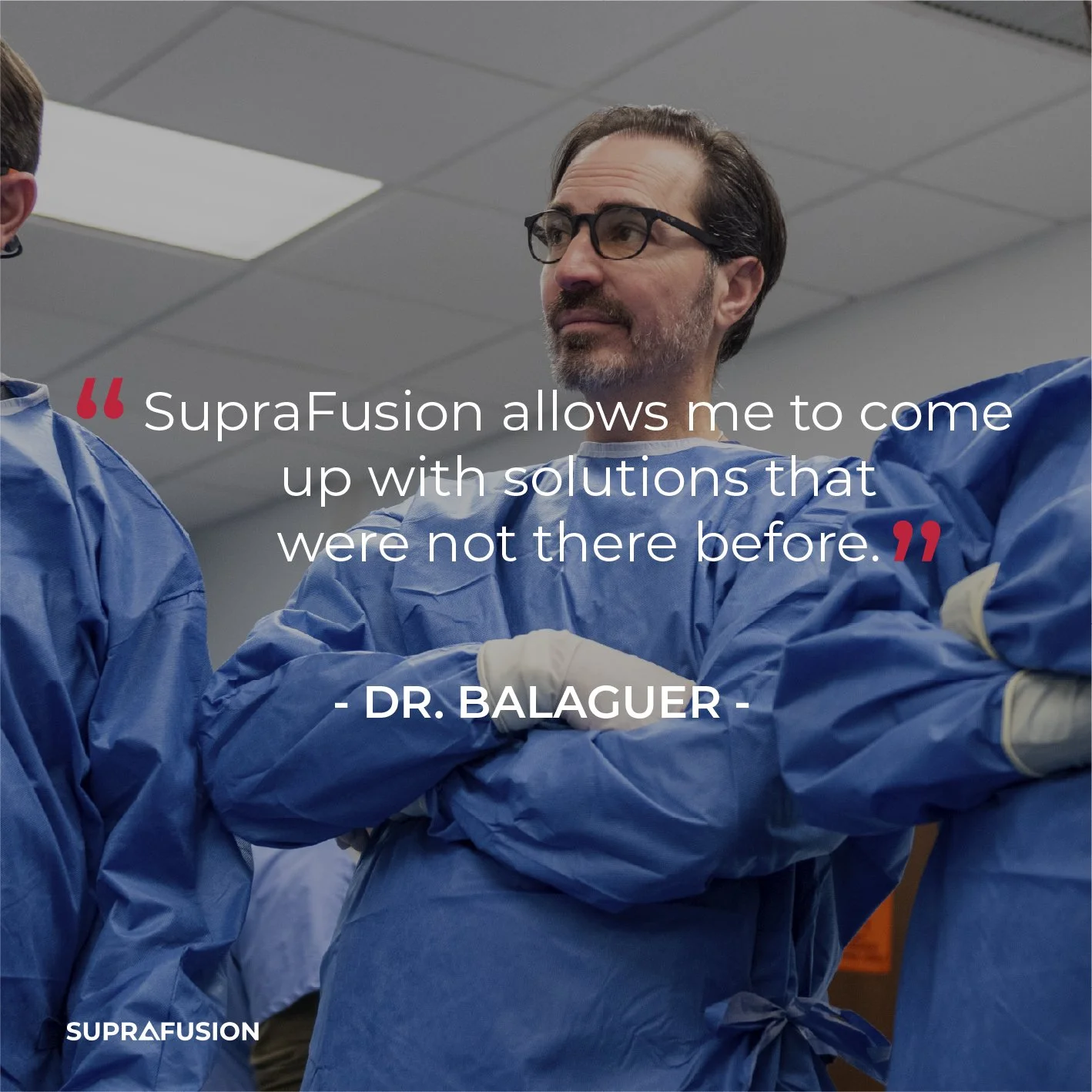 A man in blue medical scrubs and glasses, standing with arms crossed, is in a medical or clinical setting.