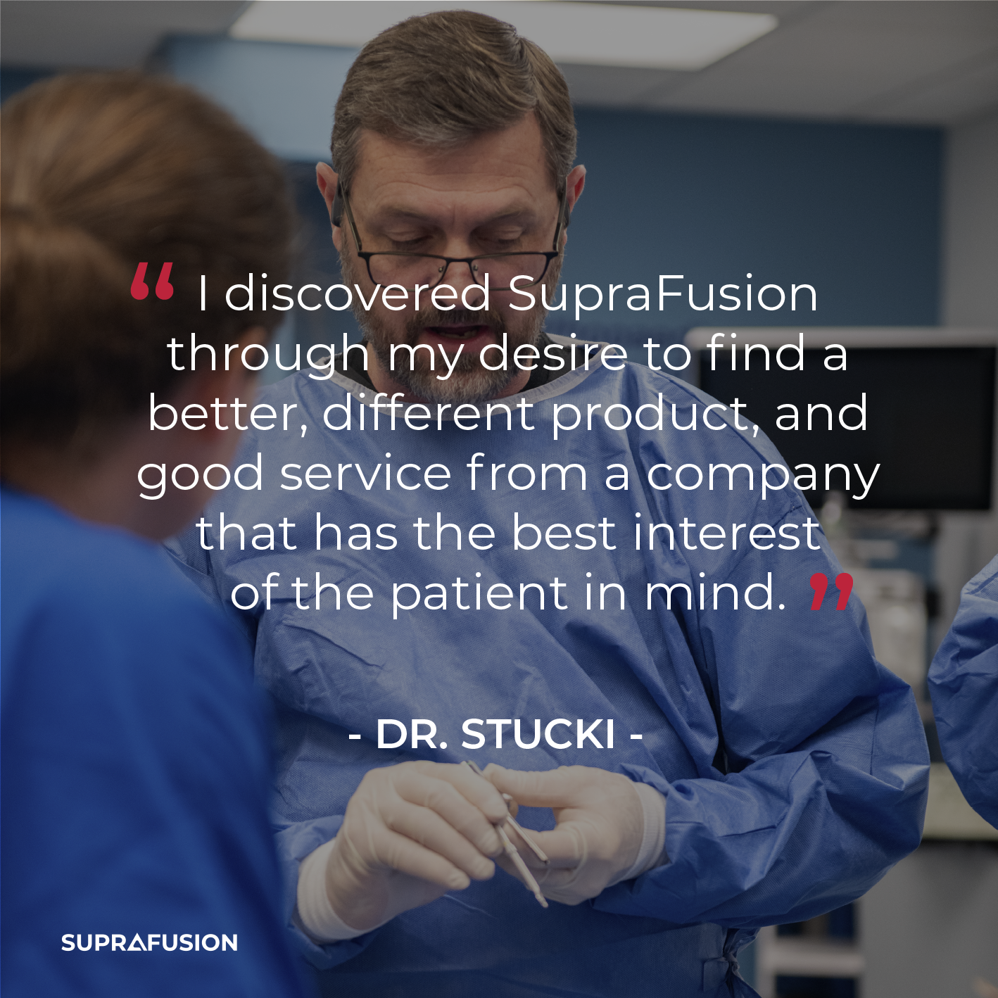 A male doctor or medical professional in a blue gown and glasses speaks to a woman in a similar gown in a clinical or hospital setting, with medical equipment and monitors in the background.