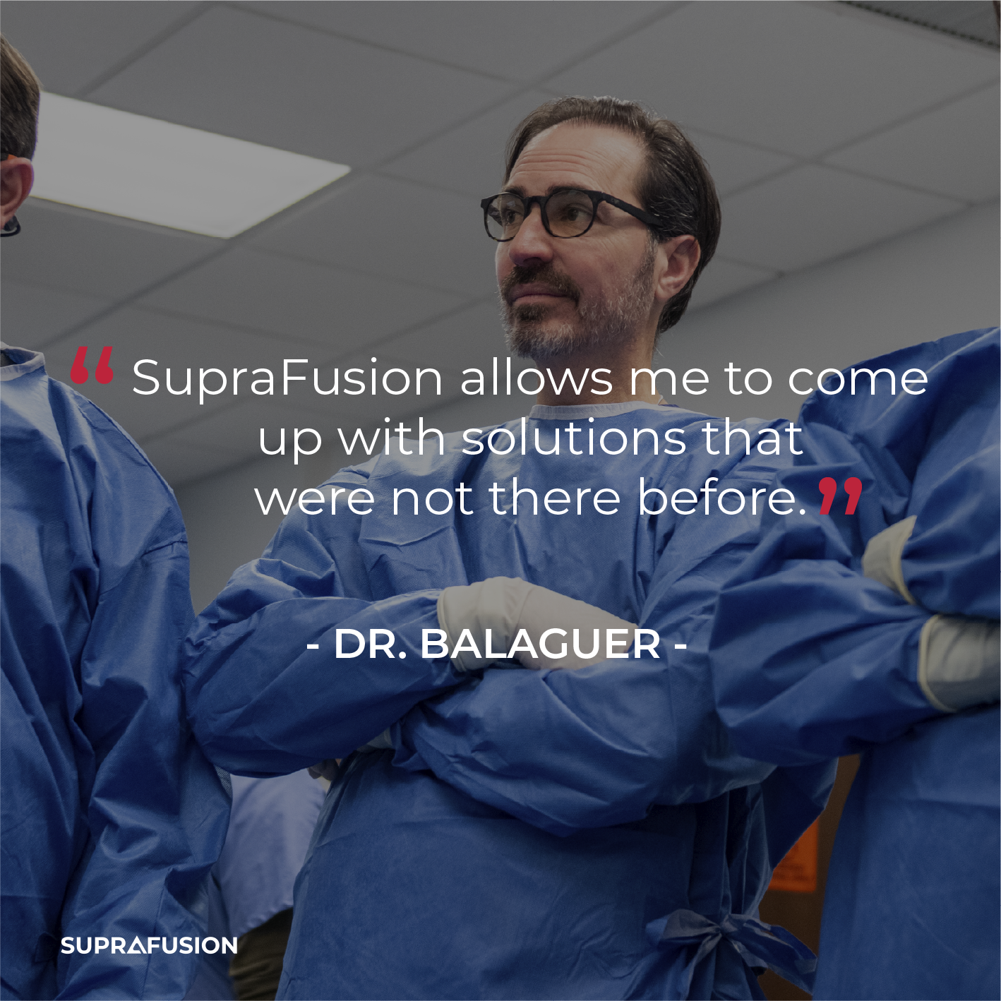 A man in blue medical scrubs and glasses, standing with arms crossed, is in a medical or clinical setting.