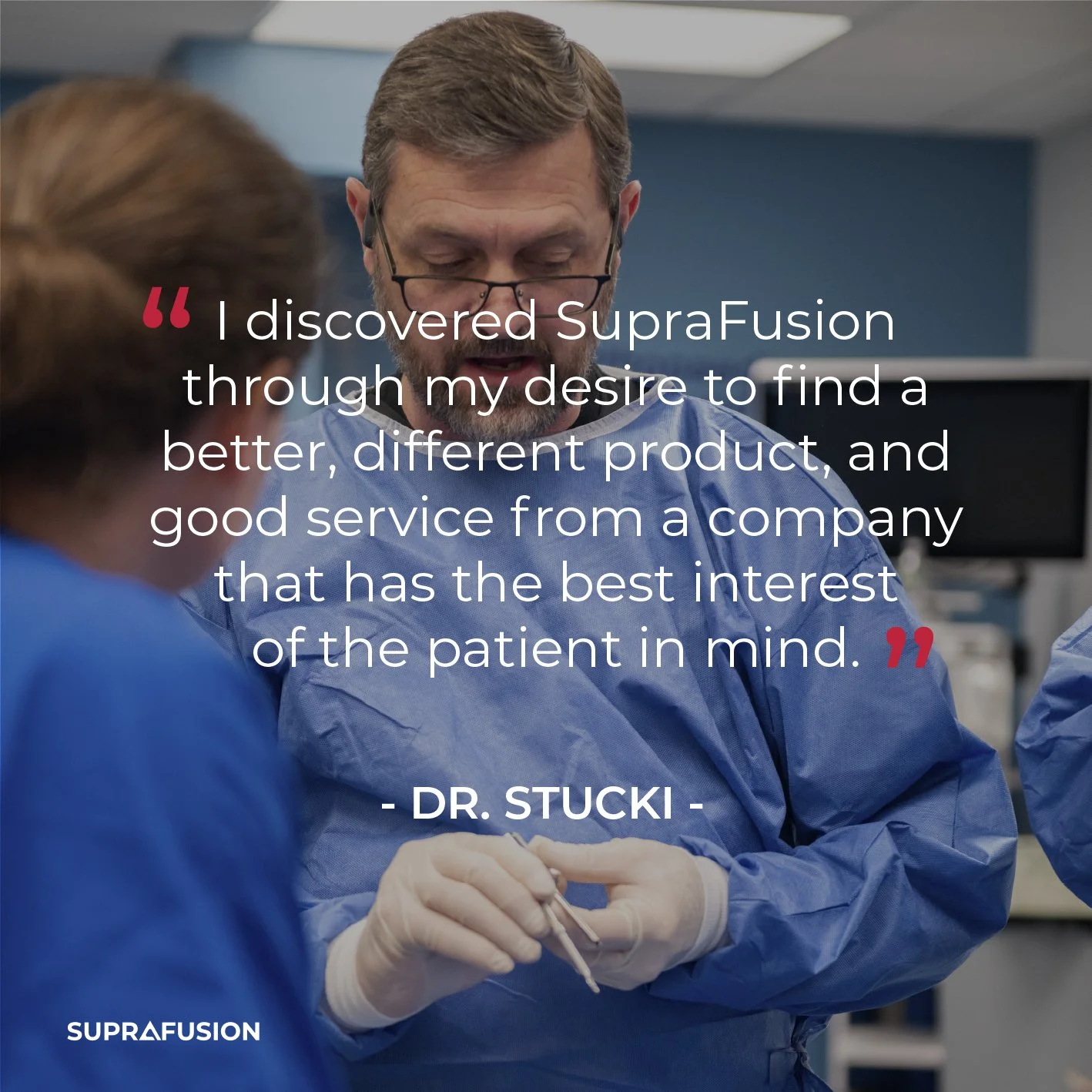 A male doctor or medical professional in a blue gown and glasses speaks to a woman in a similar gown in a clinical or hospital setting, with medical equipment and monitors in the background.