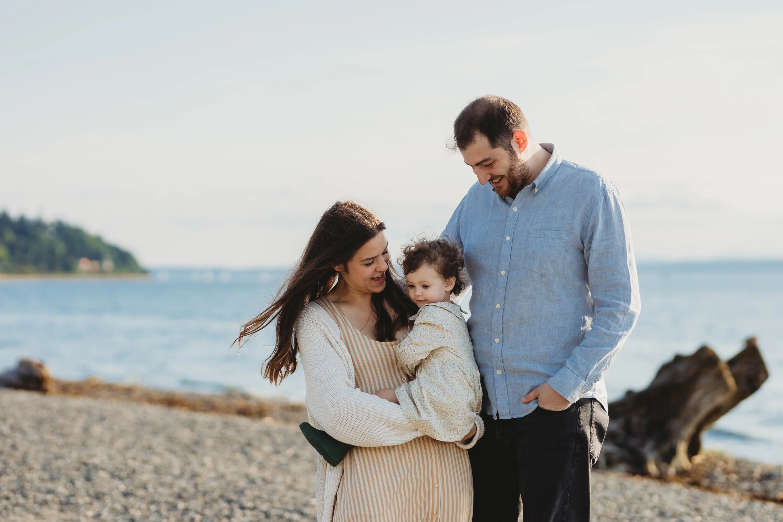 Parents holding their toddler during a relaxed family photo session at Lincoln Park by the beach in Seattle.