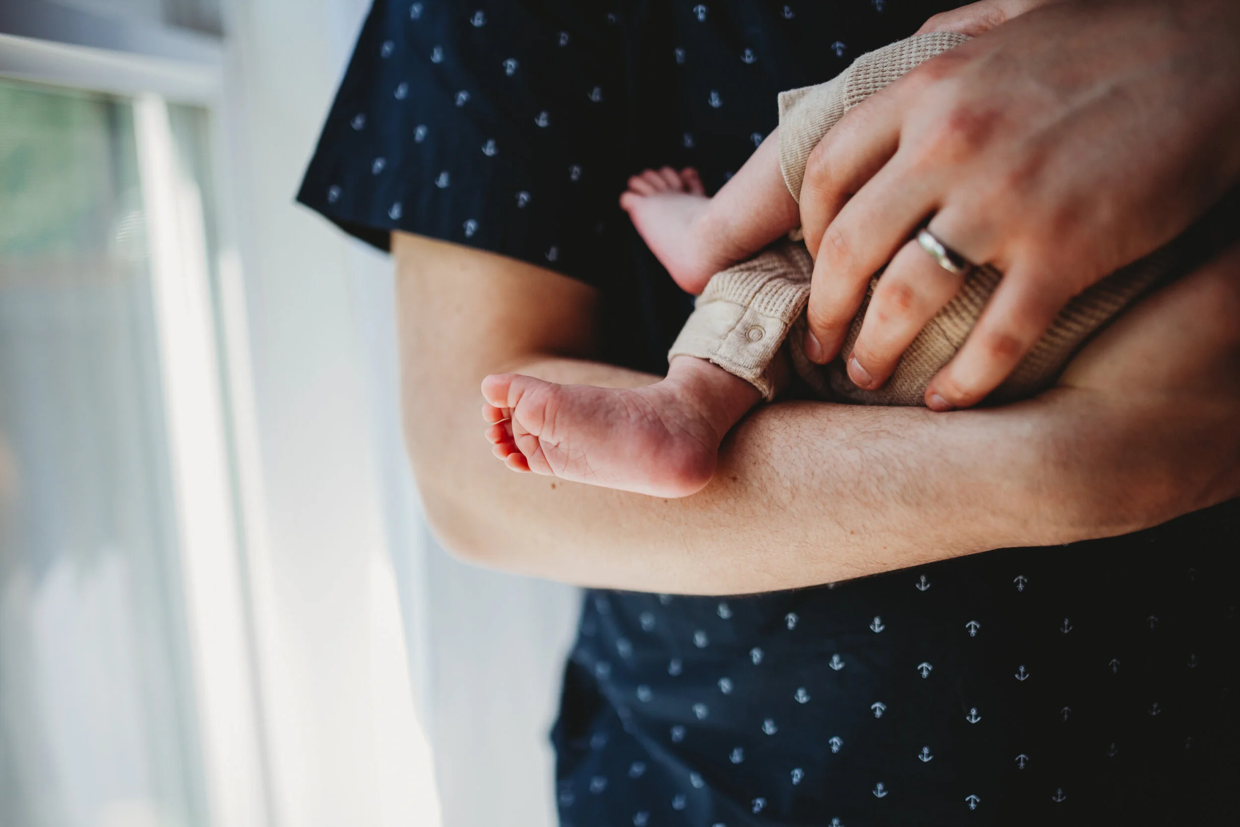 Close-up of a newborn’s feet resting in a parent’s arms during an in-home photo session in Seattle.