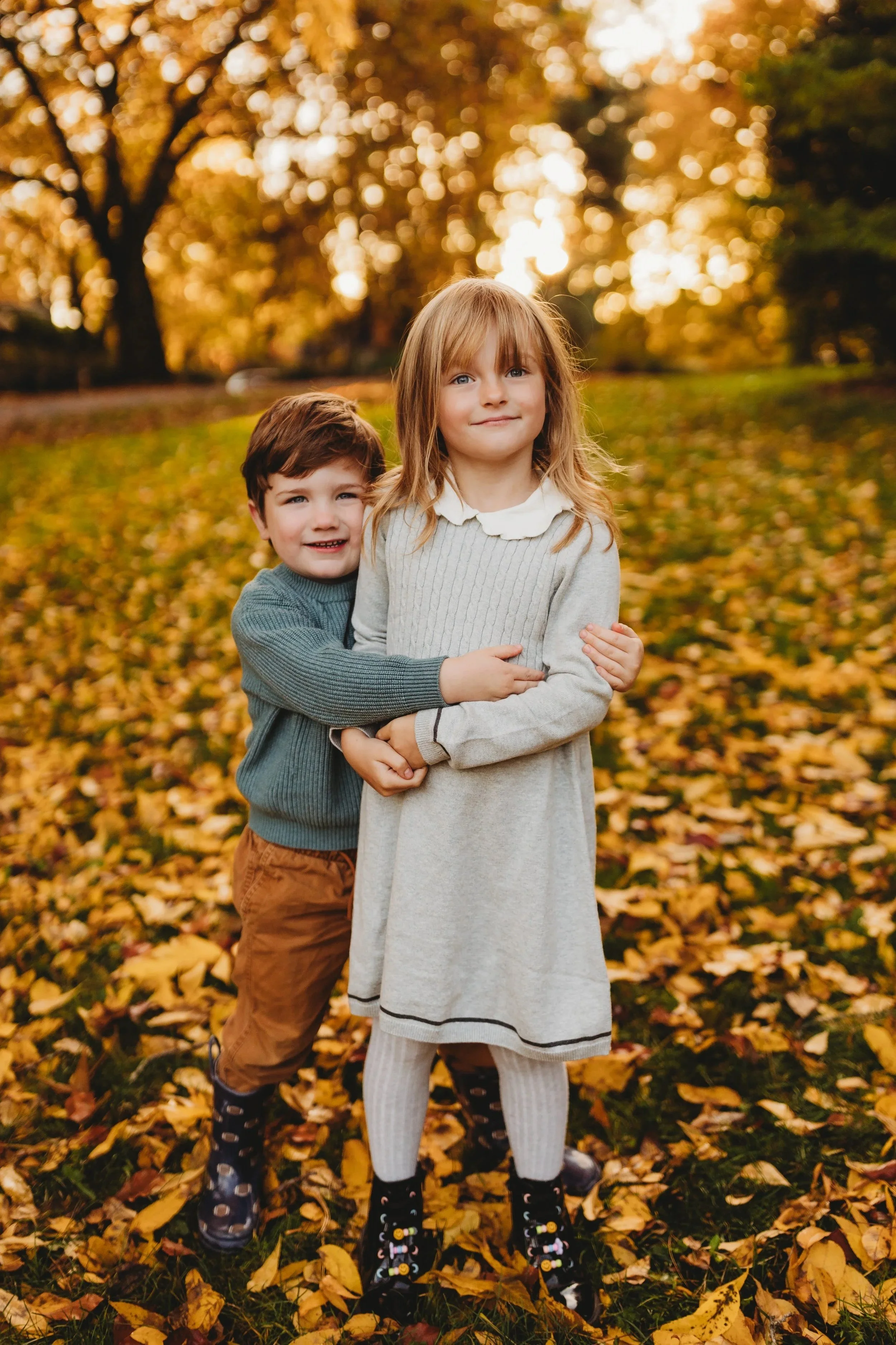 Two siblings in coordinated fall outfits standing in golden leaves during Seattle family mini session