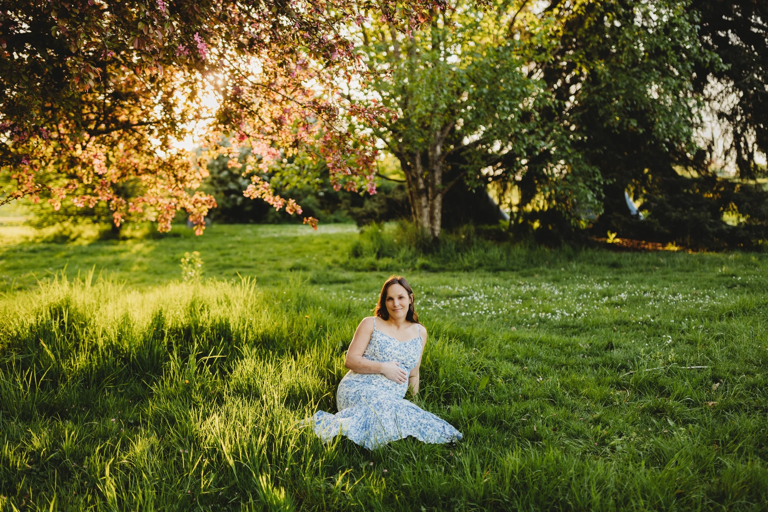 Pregnant woman seated in a grassy field at Magnuson Park during a maternity photo session in Seattle.
