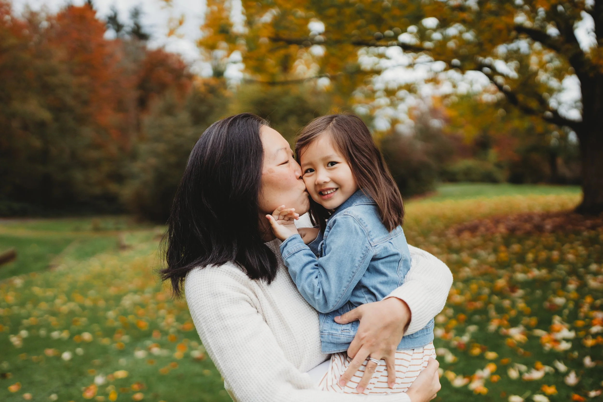 Parent holding and kissing their child during a natural light family photo session at Luther Burbank Park on Mercer Island.