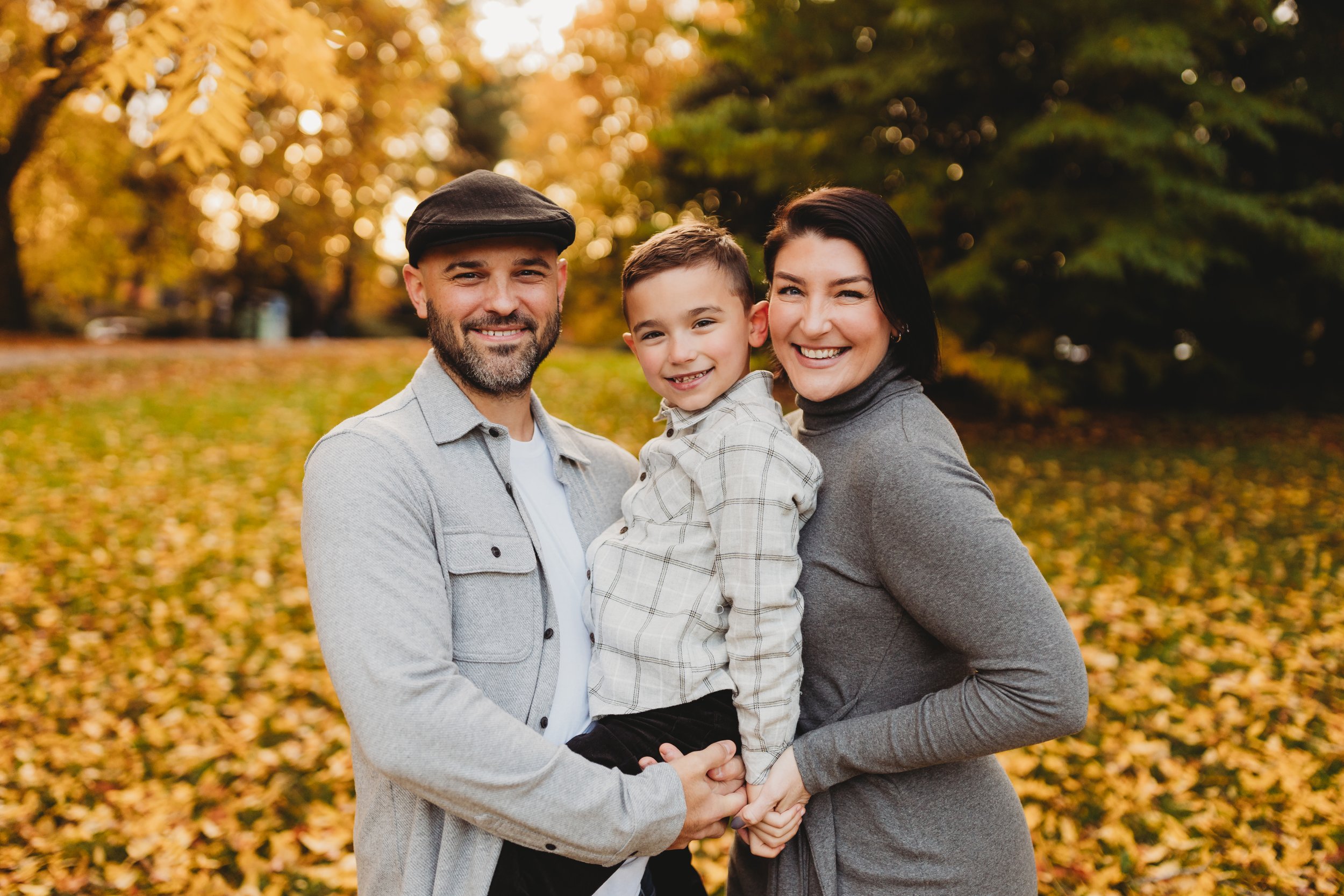 Family of three smiling together at golden hour, Volunteer Park fall mini session, Seattle photographer
